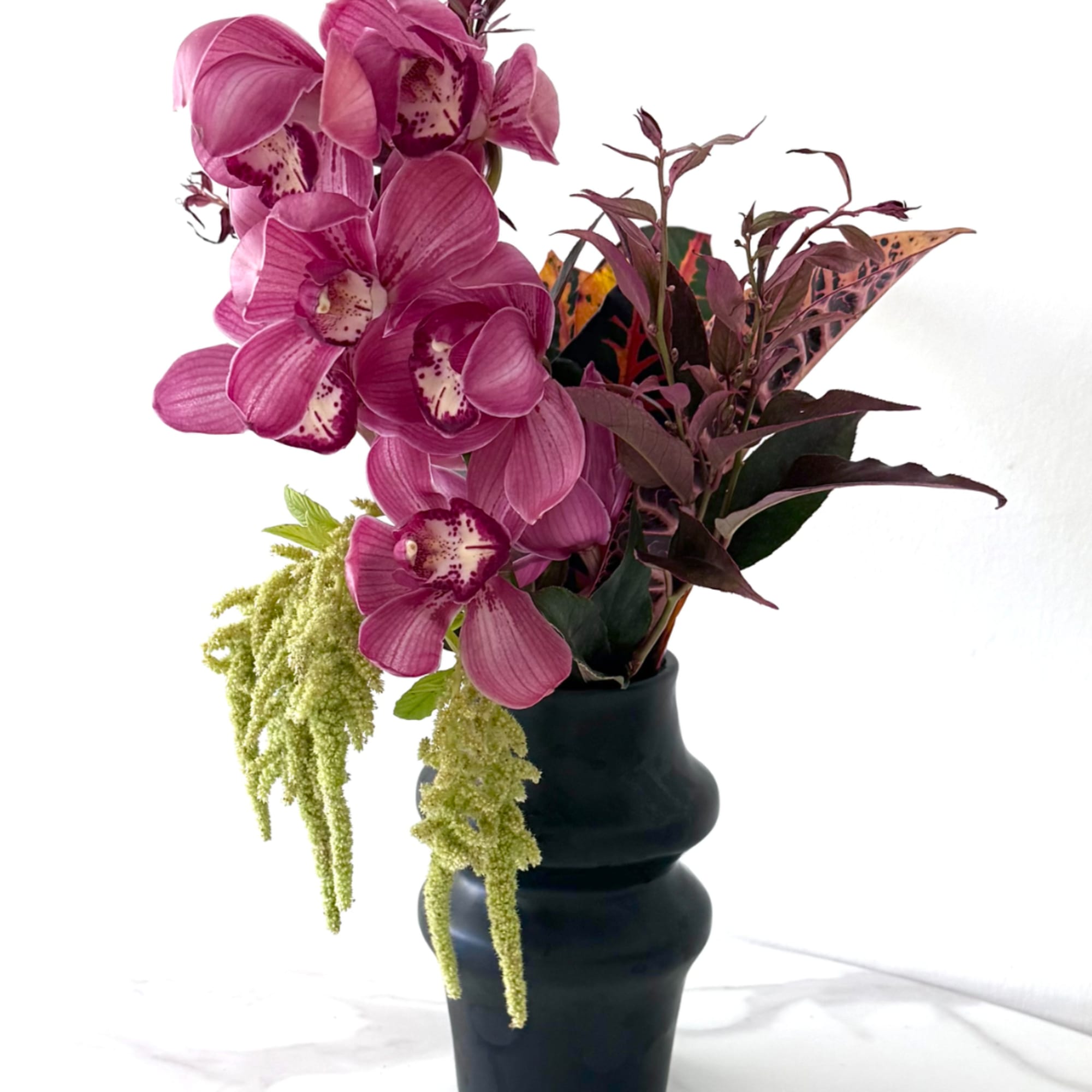 Pink orchids arranged in a dark vase with trailing green filler