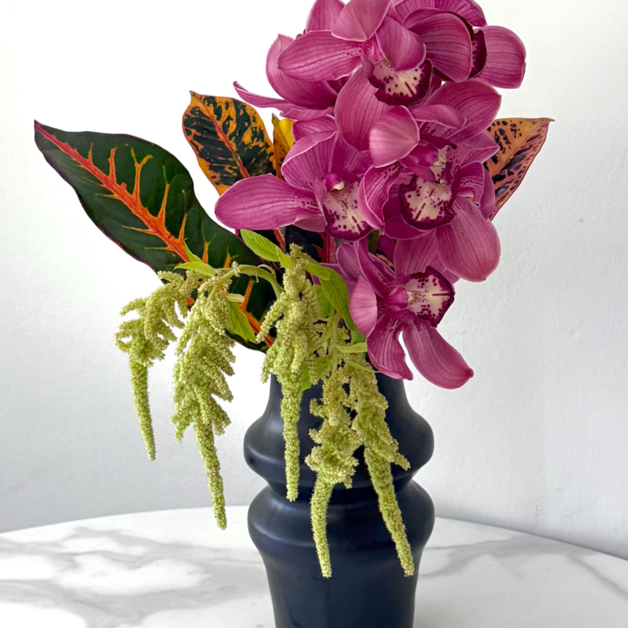 Magenta orchids in a dark vase with variegated tropical leaves