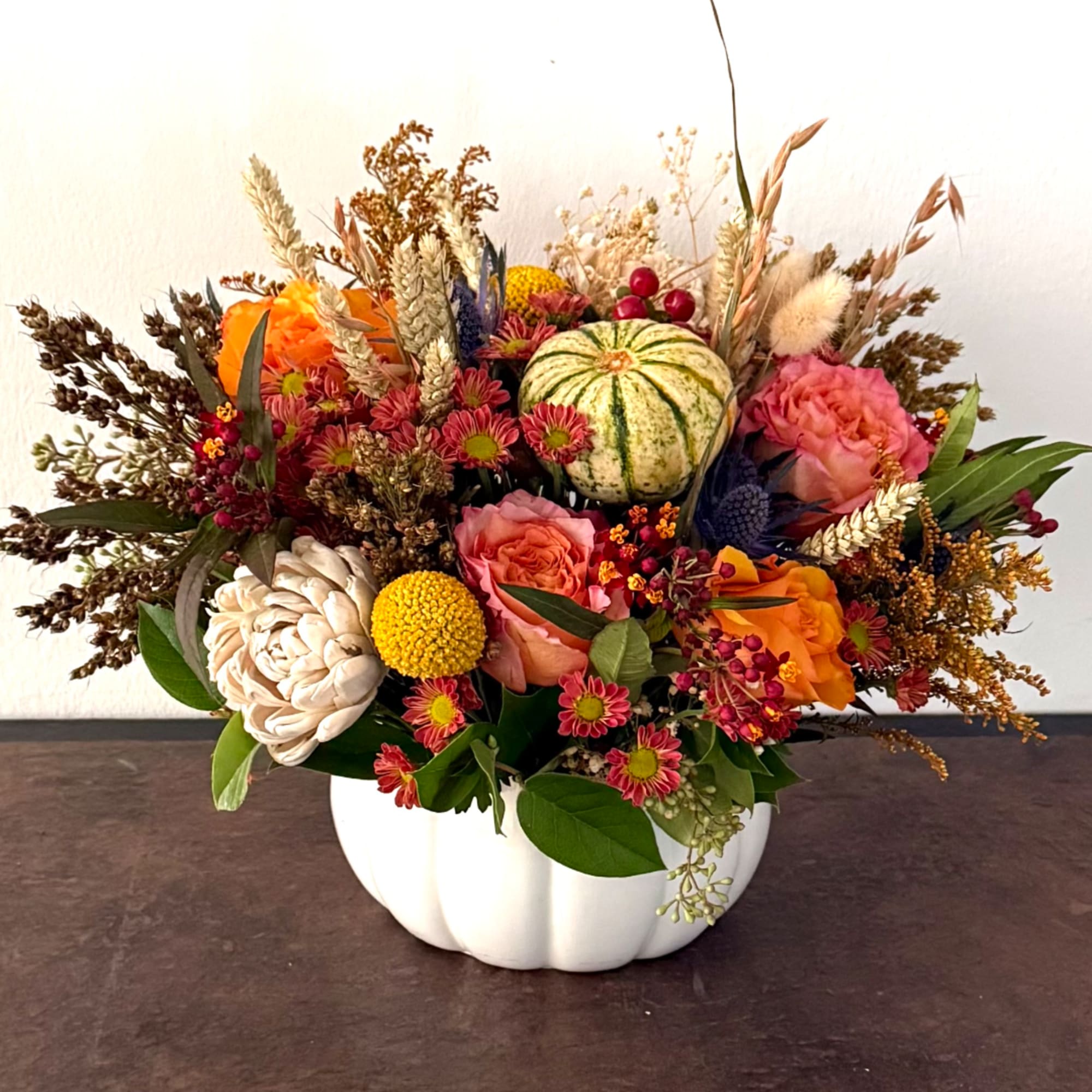 Autumn floral arrangement in a white pumpkin vase with orange and pink blooms