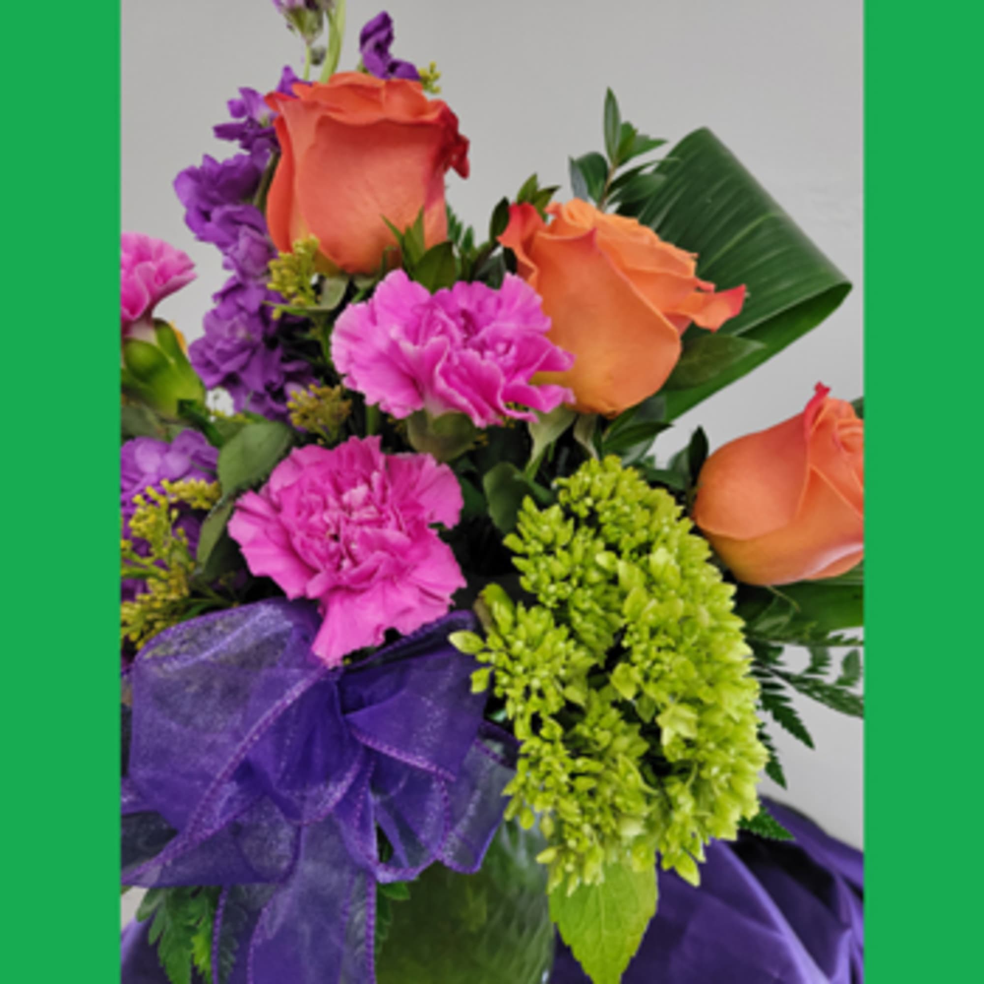 Bouquet of orange roses, pink carnations, and purple flowers with a ribbon