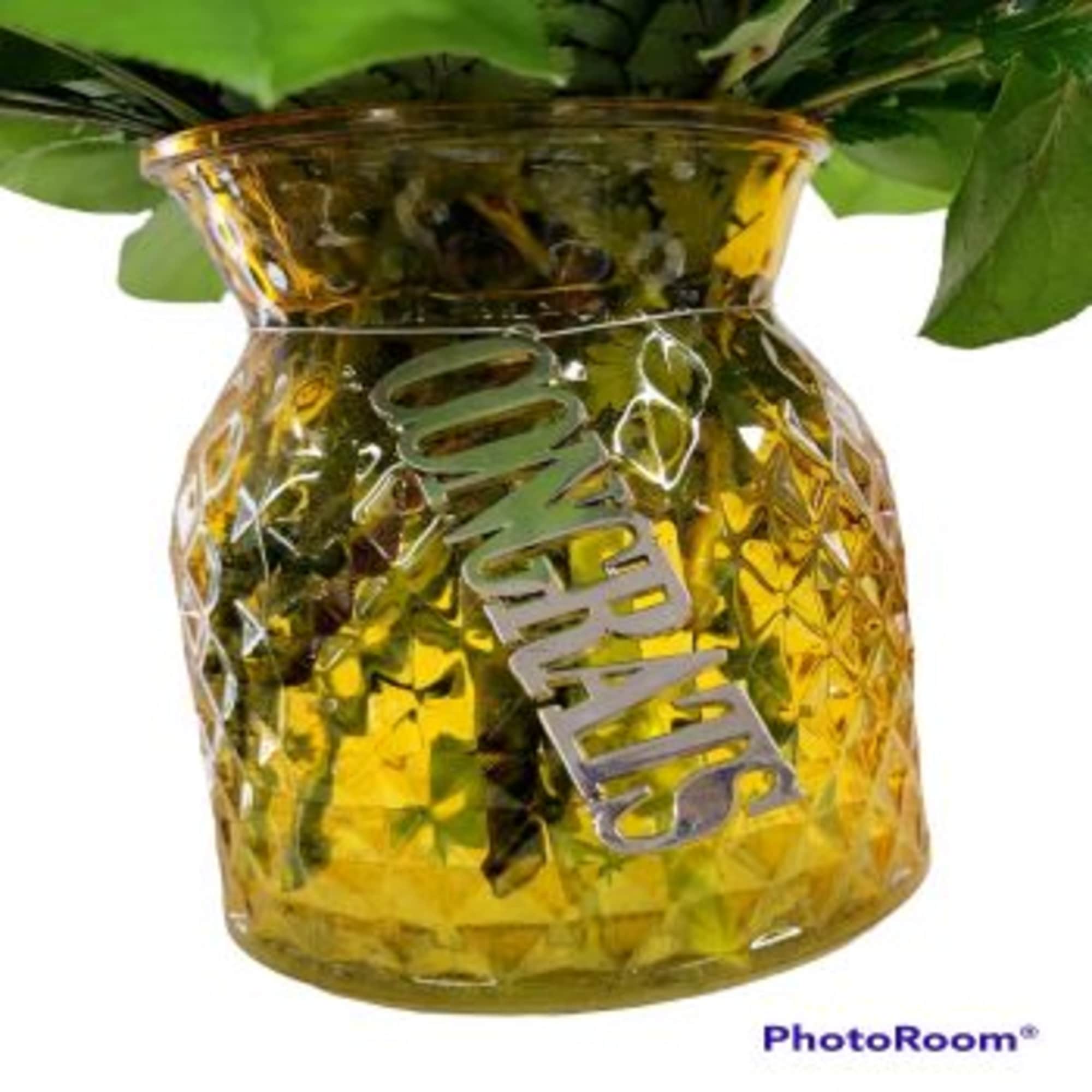 Yellow glass vase with green foliage and a silver "MOM" tag