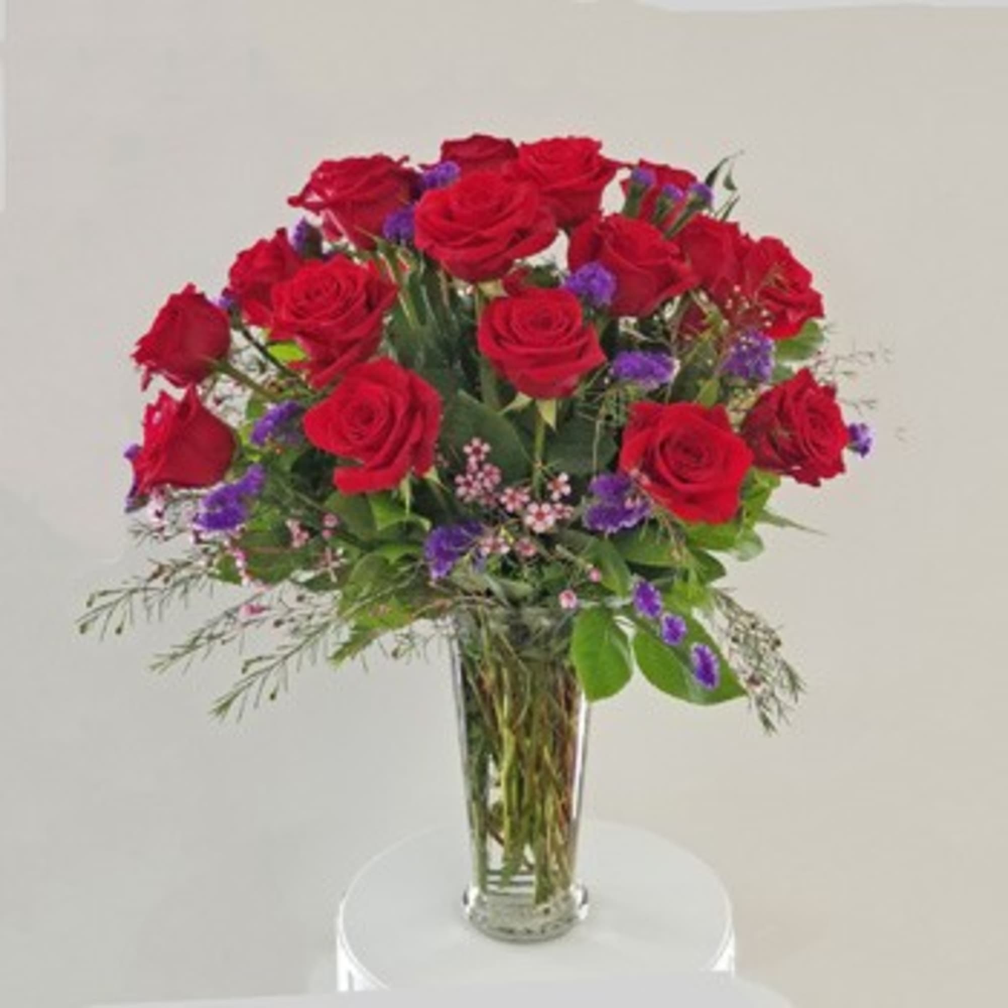 Red roses arranged in a clear glass vase with purple filler flowers