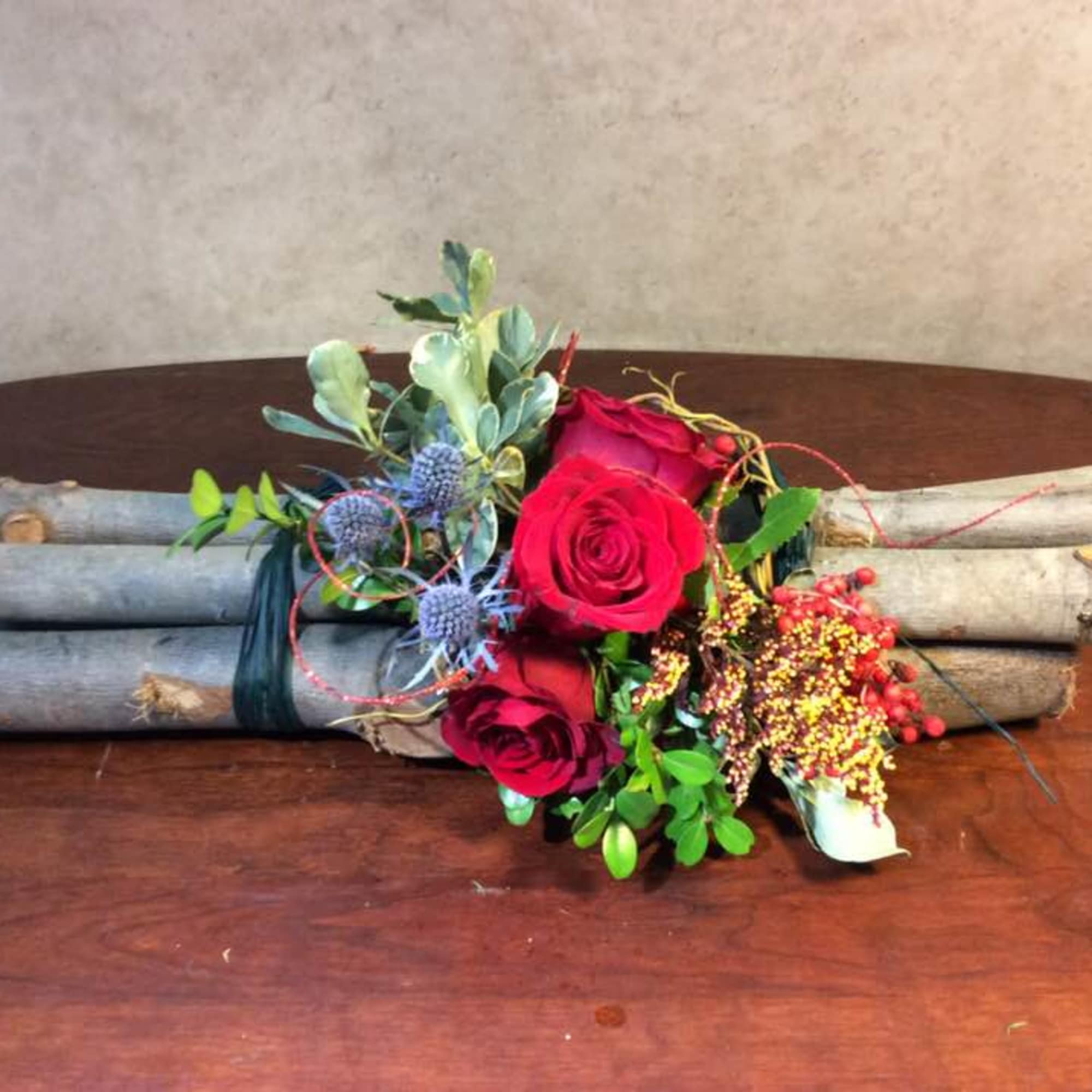 Red roses arranged with berries and greenery on bundled branches