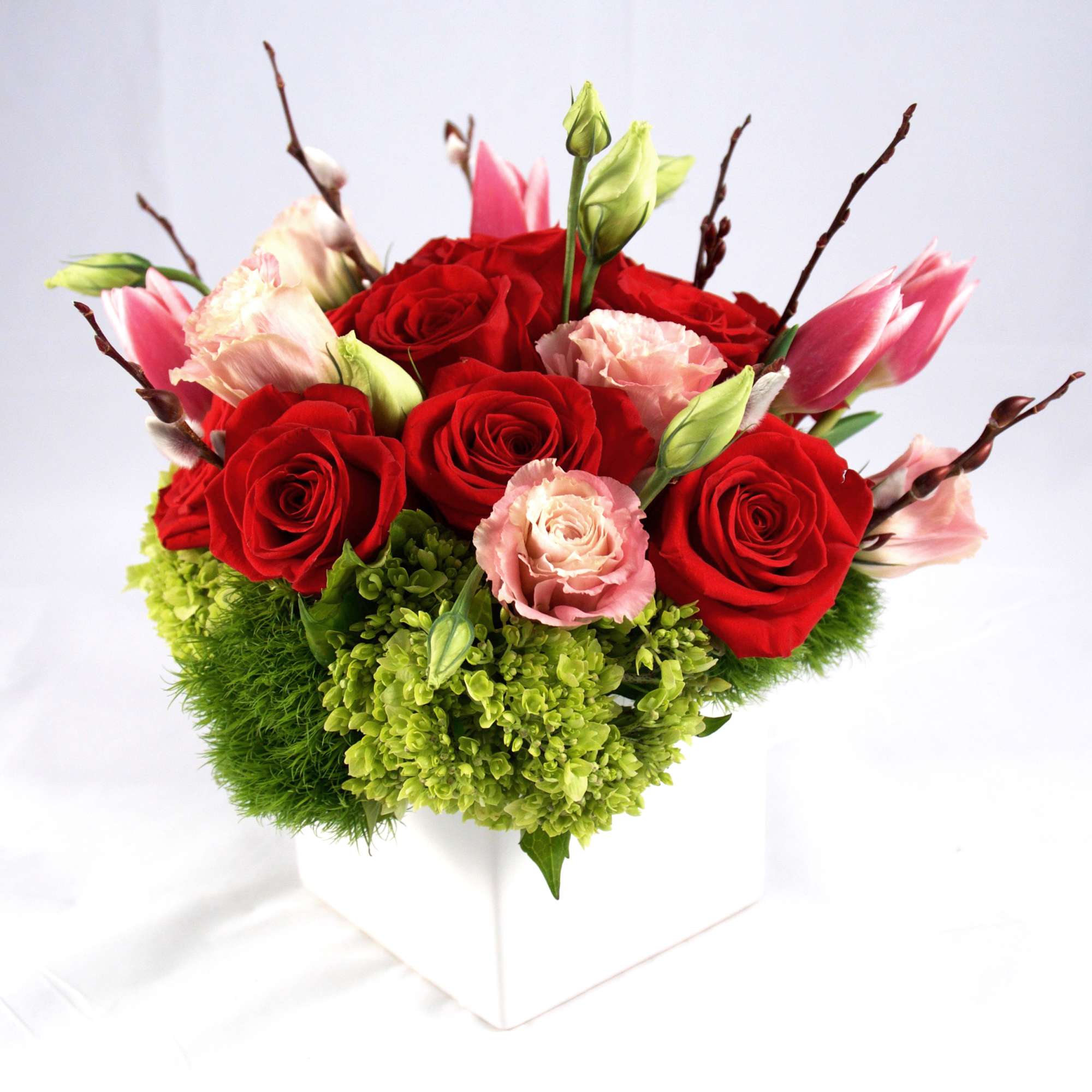 Red roses and pink blooms in a white square vase
