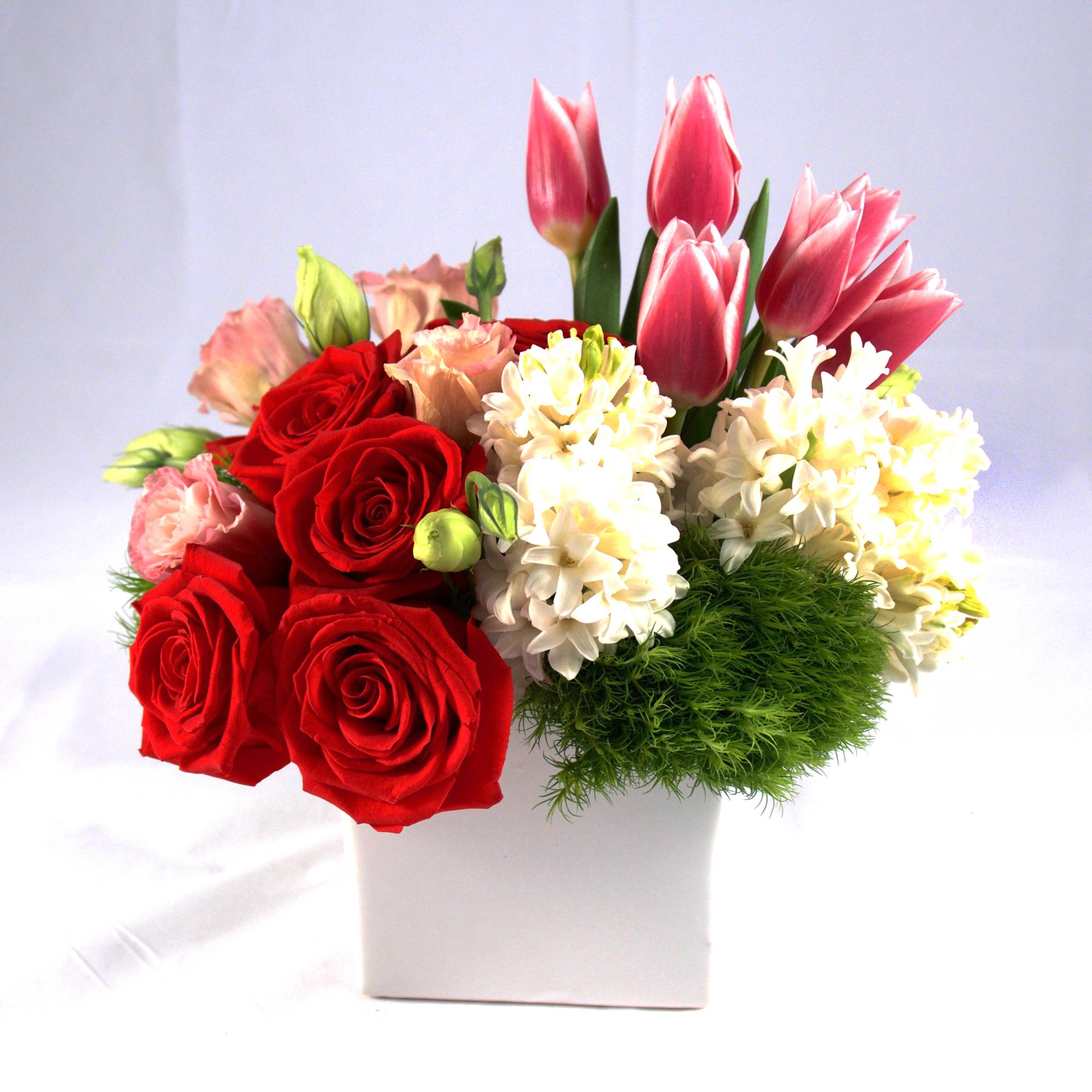 Bouquet of red roses, pink tulips, and white flowers in a white box