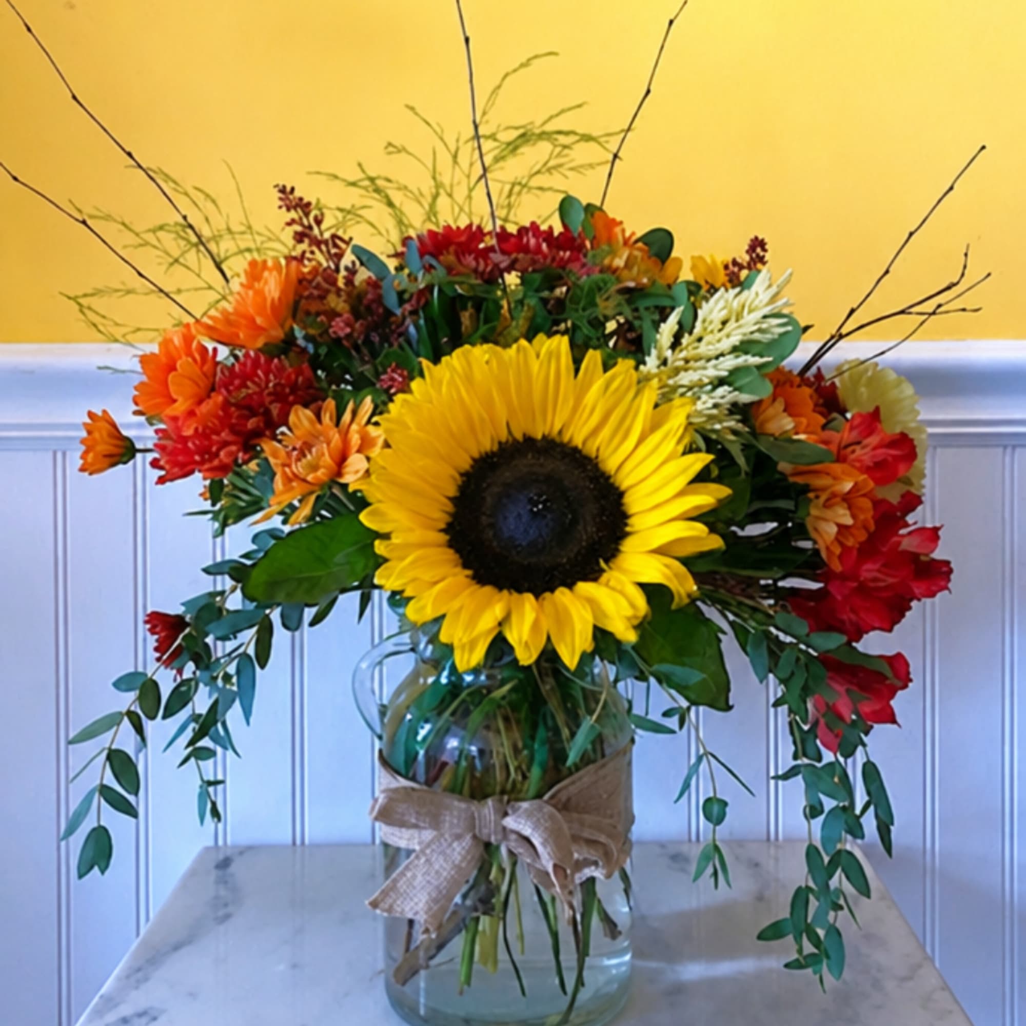 Sunflower and mixed autumn bouquet in a glass jar with a burlap bow