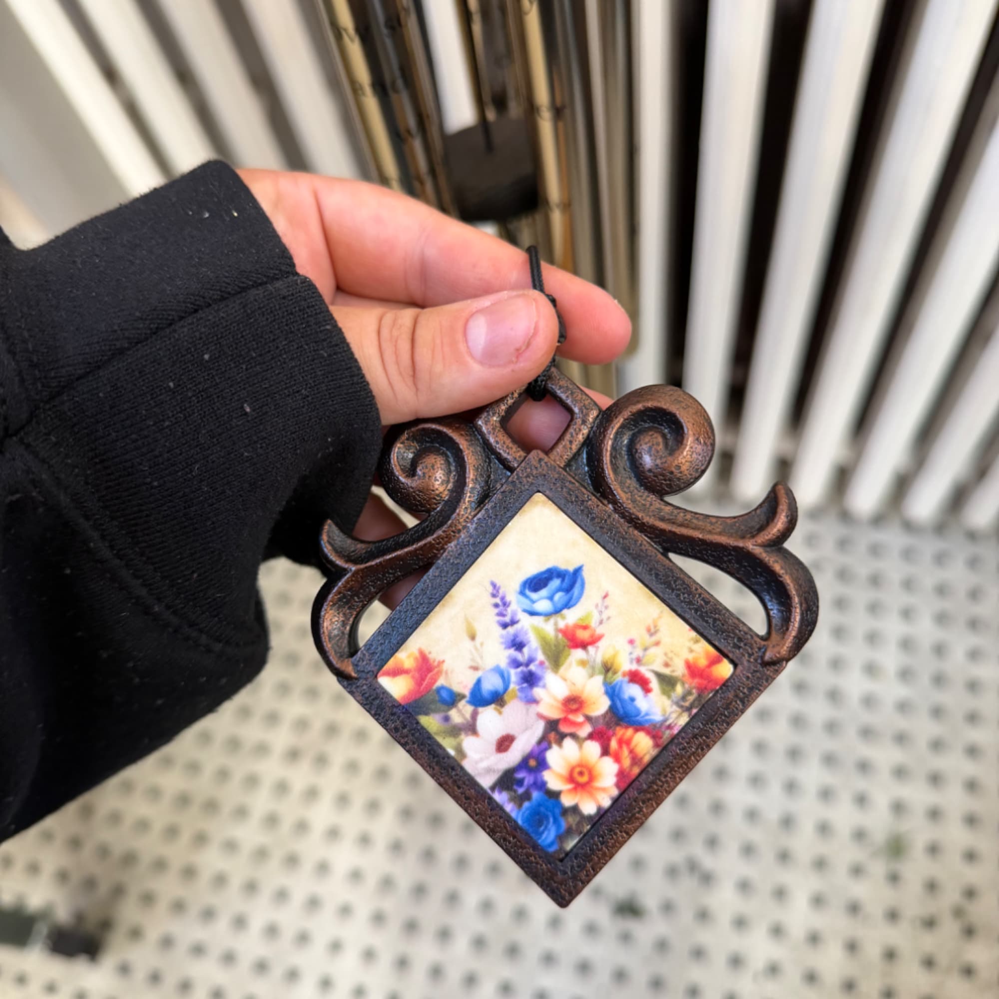 Hand holding a small decorative hanging frame with a colorful floral print