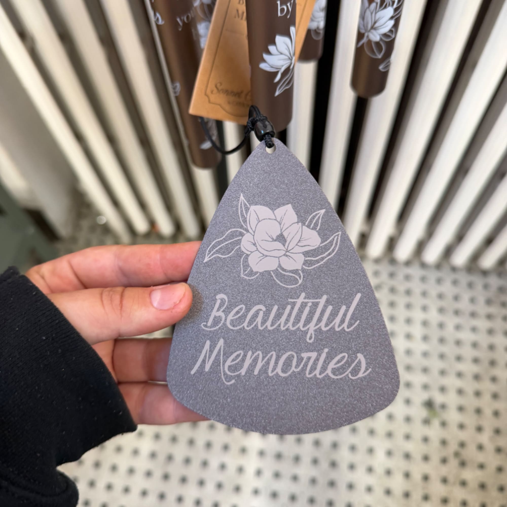 Hand holding a gray memorial tag with floral print and the words Beautiful Memories
