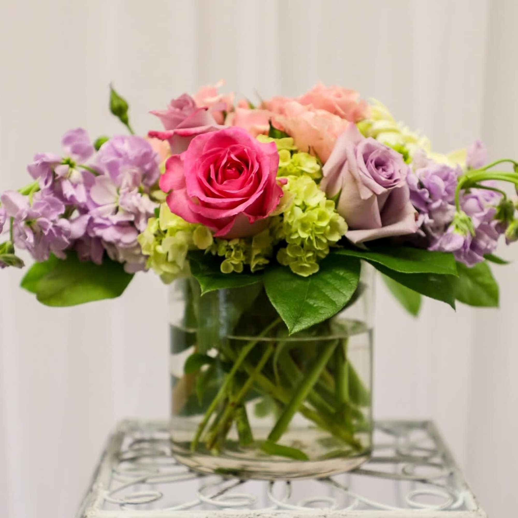 Pink and lavender roses with purple flowers in a glass vase