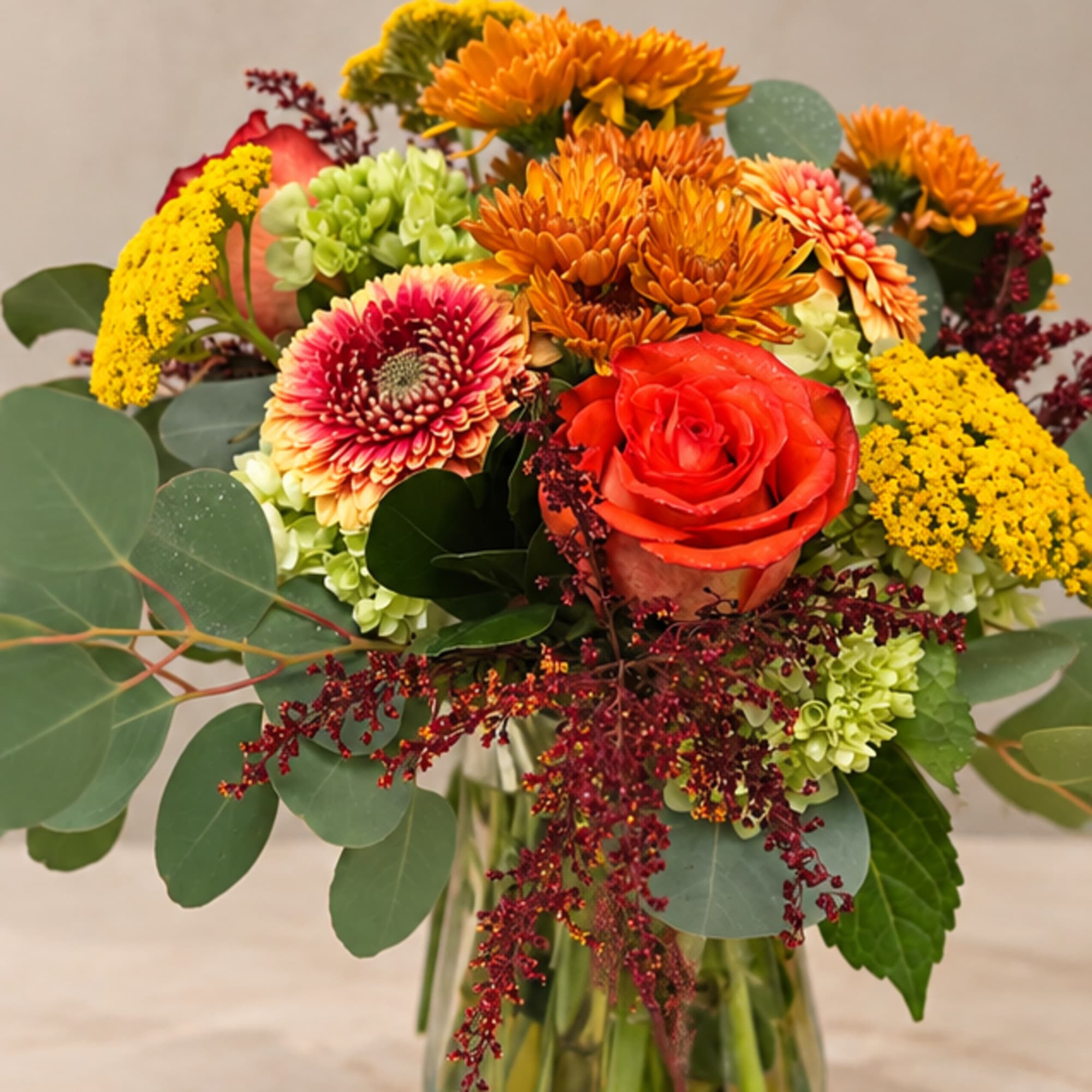 Mixed bouquet of orange, red, and yellow flowers in a clear glass vase