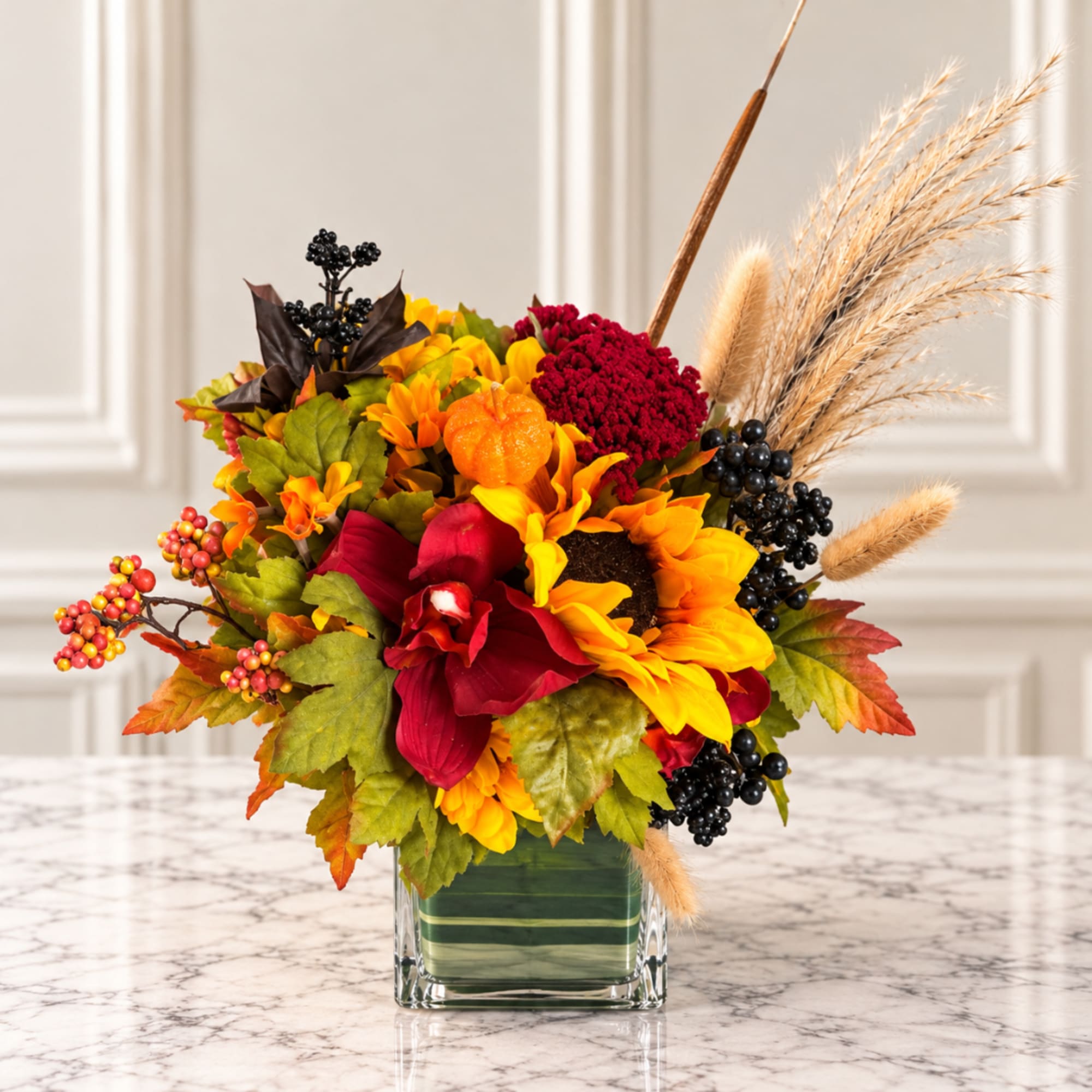 Autumn floral arrangement with sunflowers and red blooms in a square glass vase