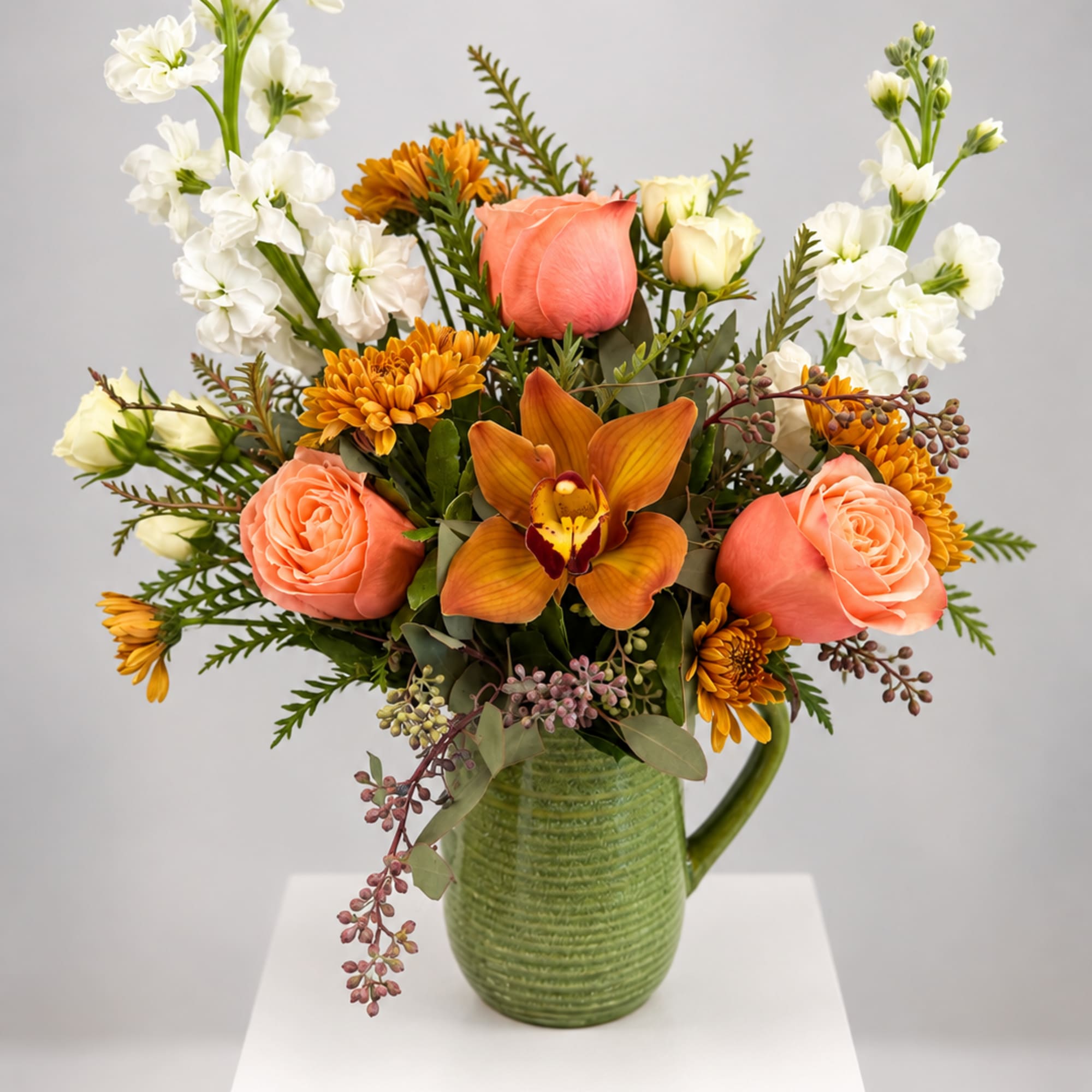 Peach roses and orange blooms in a green ceramic pitcher