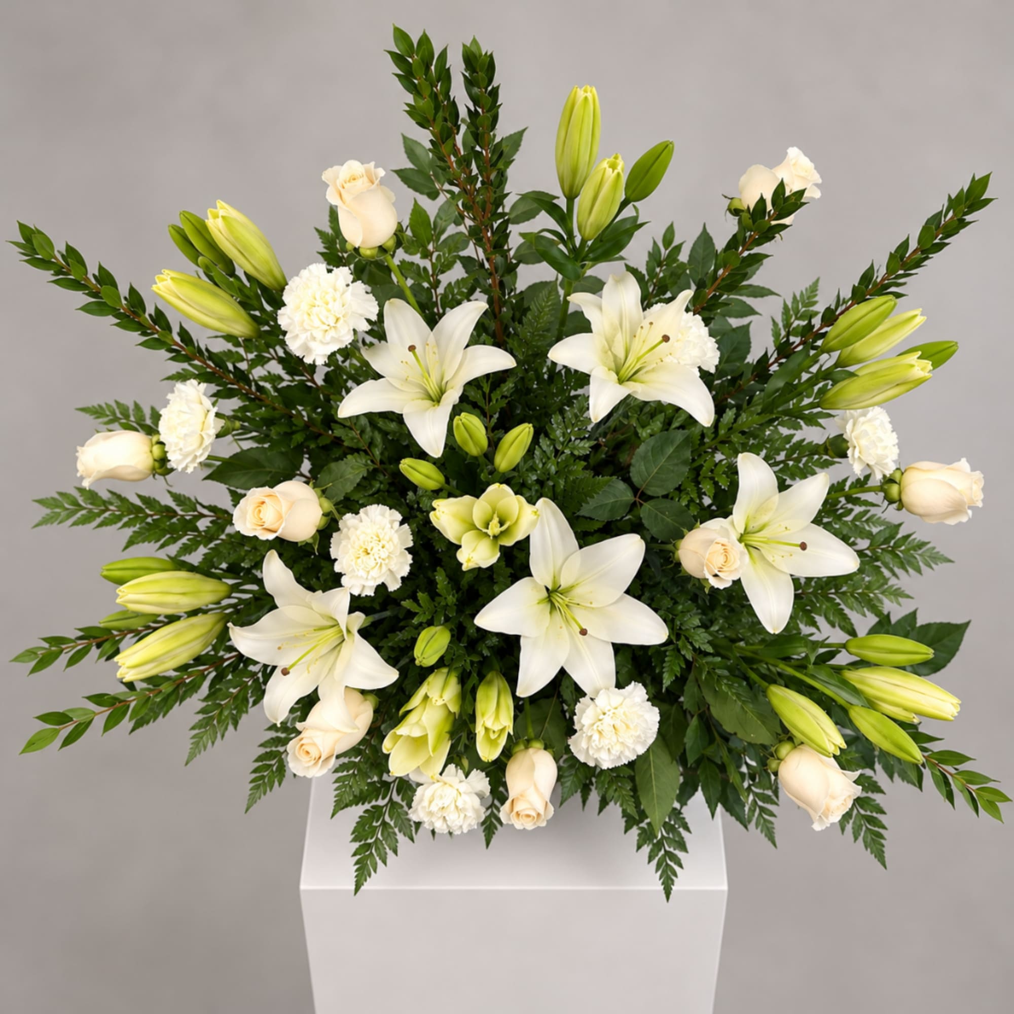 White lilies and cream roses arranged in a square vase with greenery