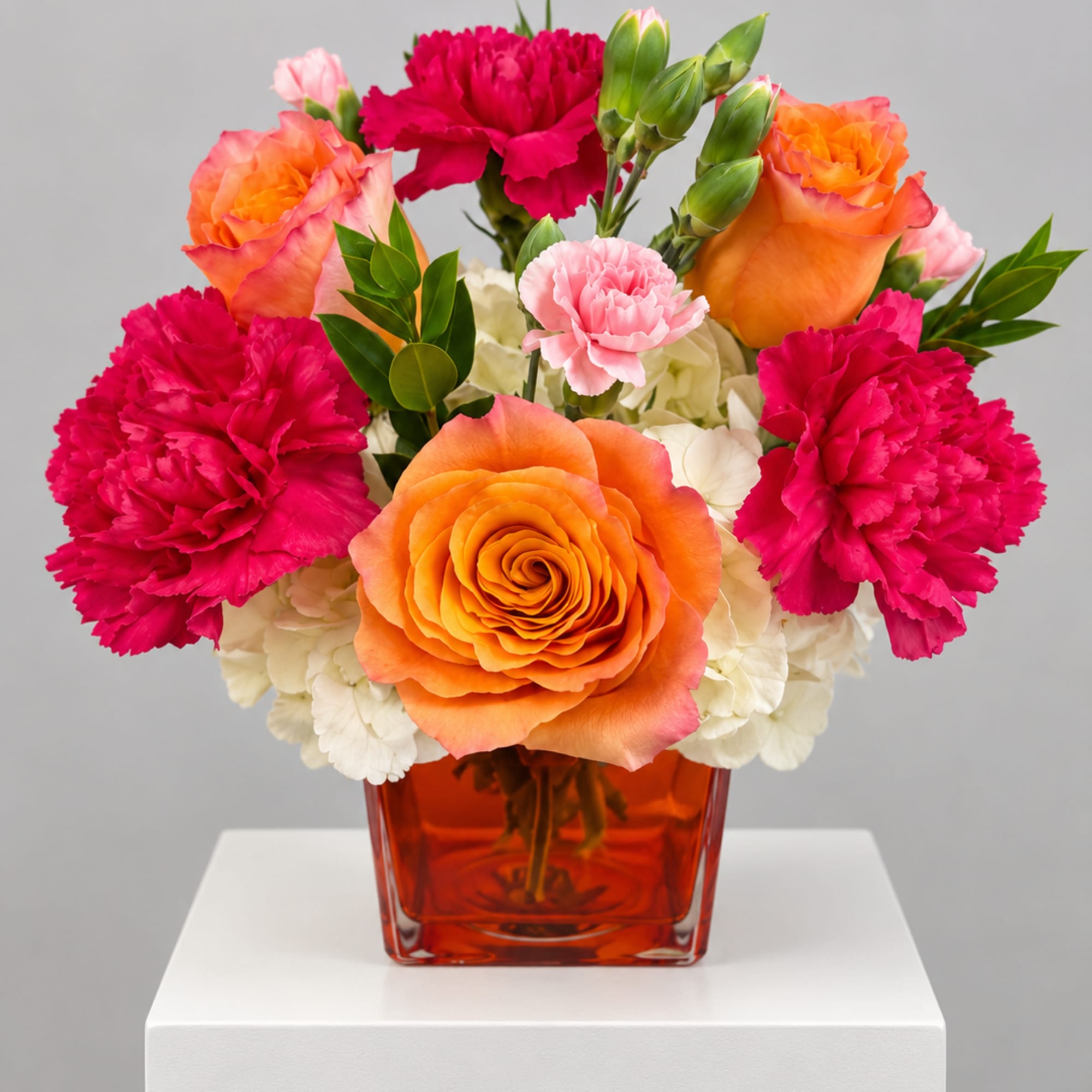 Orange roses and pink carnations in a red glass vase