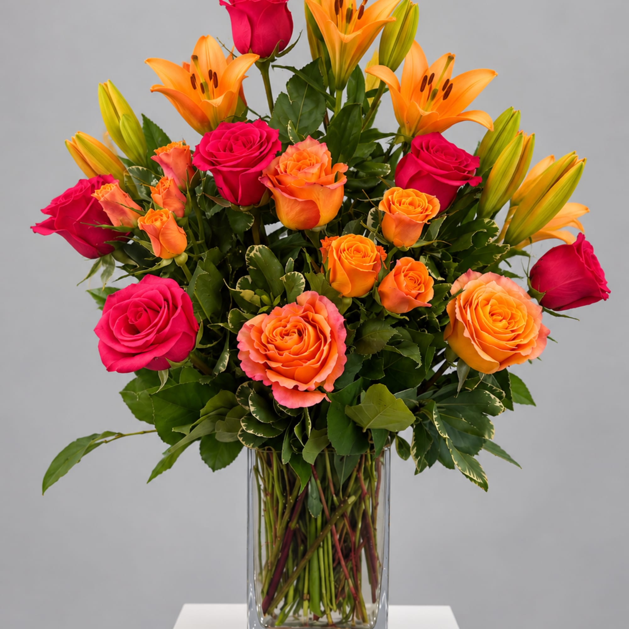 Pink and orange roses with orange lilies in a glass vase