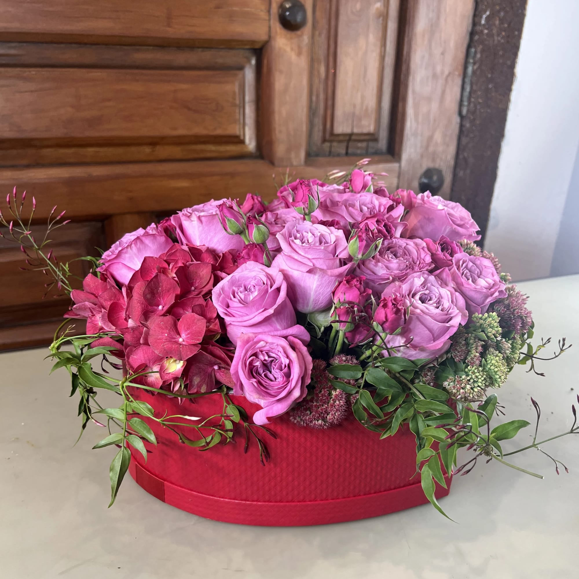 Pink roses and hydrangeas arranged in a red hat box