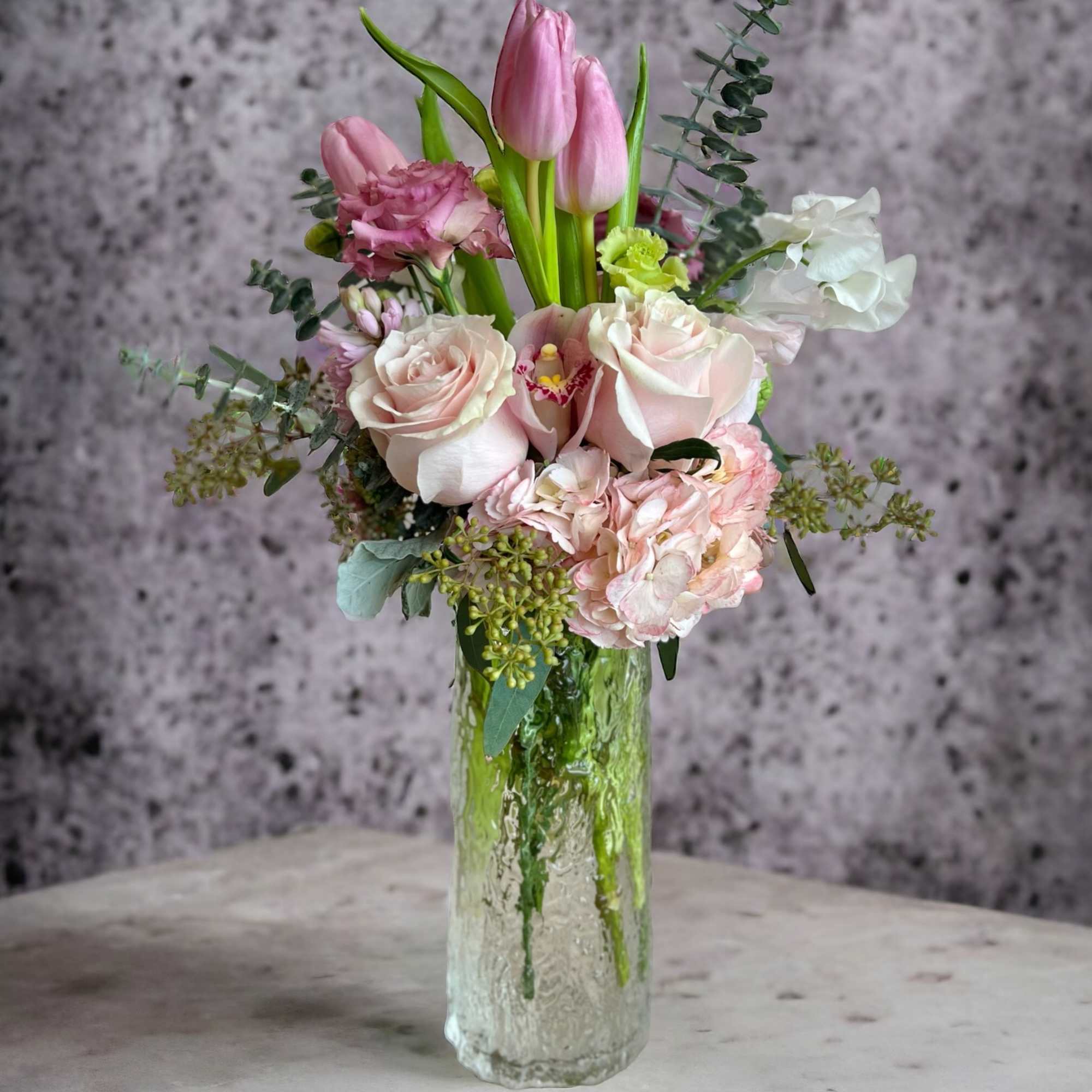 Pink tulips and pale roses arranged in a clear glass vase