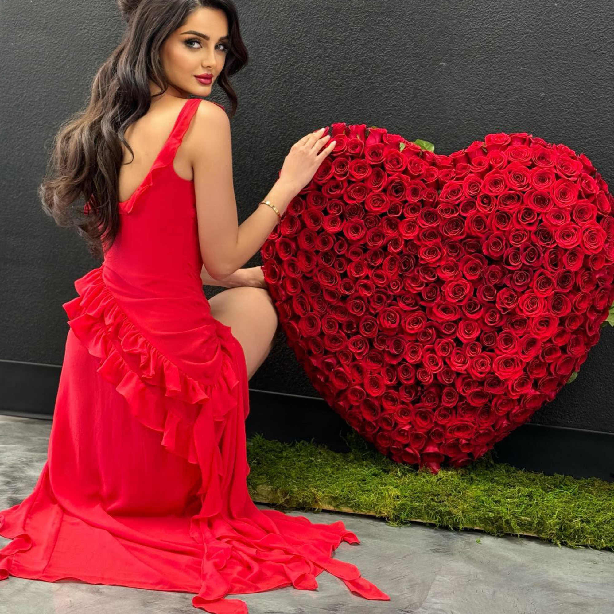 Woman in a red dress posing beside a large heart-shaped rose display