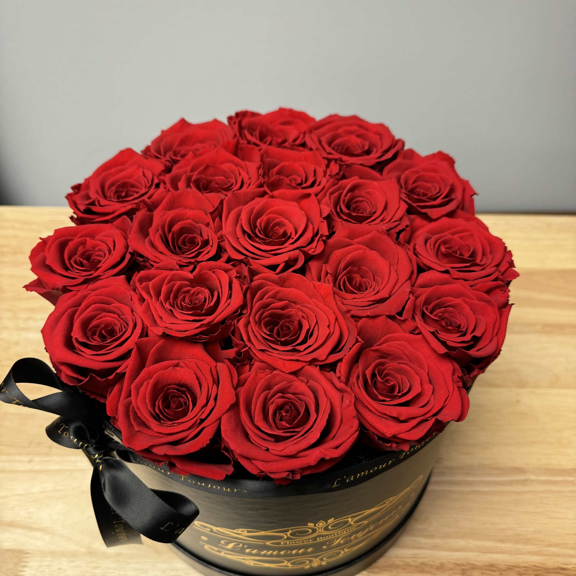 Round arrangement of red roses in a black hatbox with a black ribbon bow.