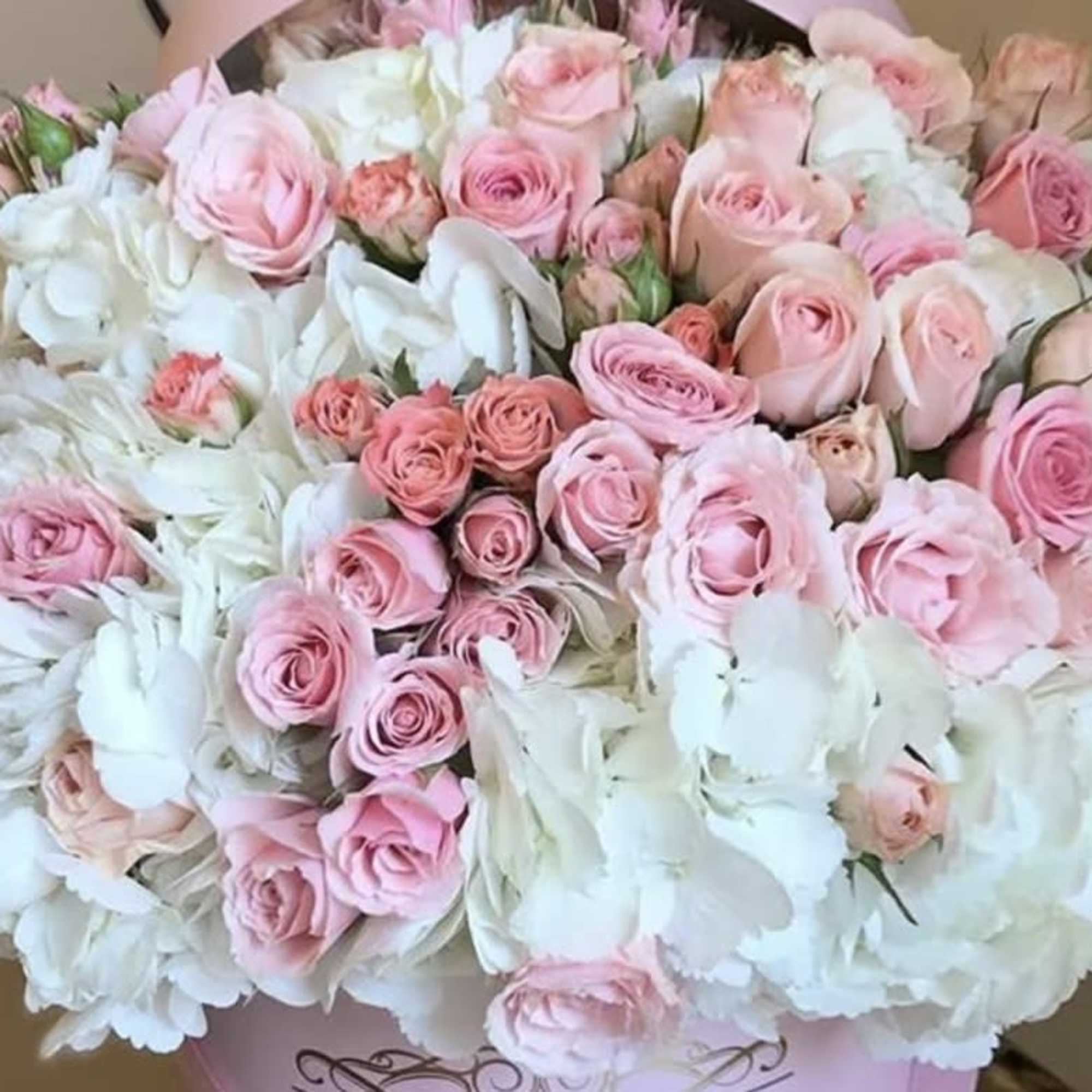 Large round arrangement of pink roses and white hydrangeas in a pale hatbox