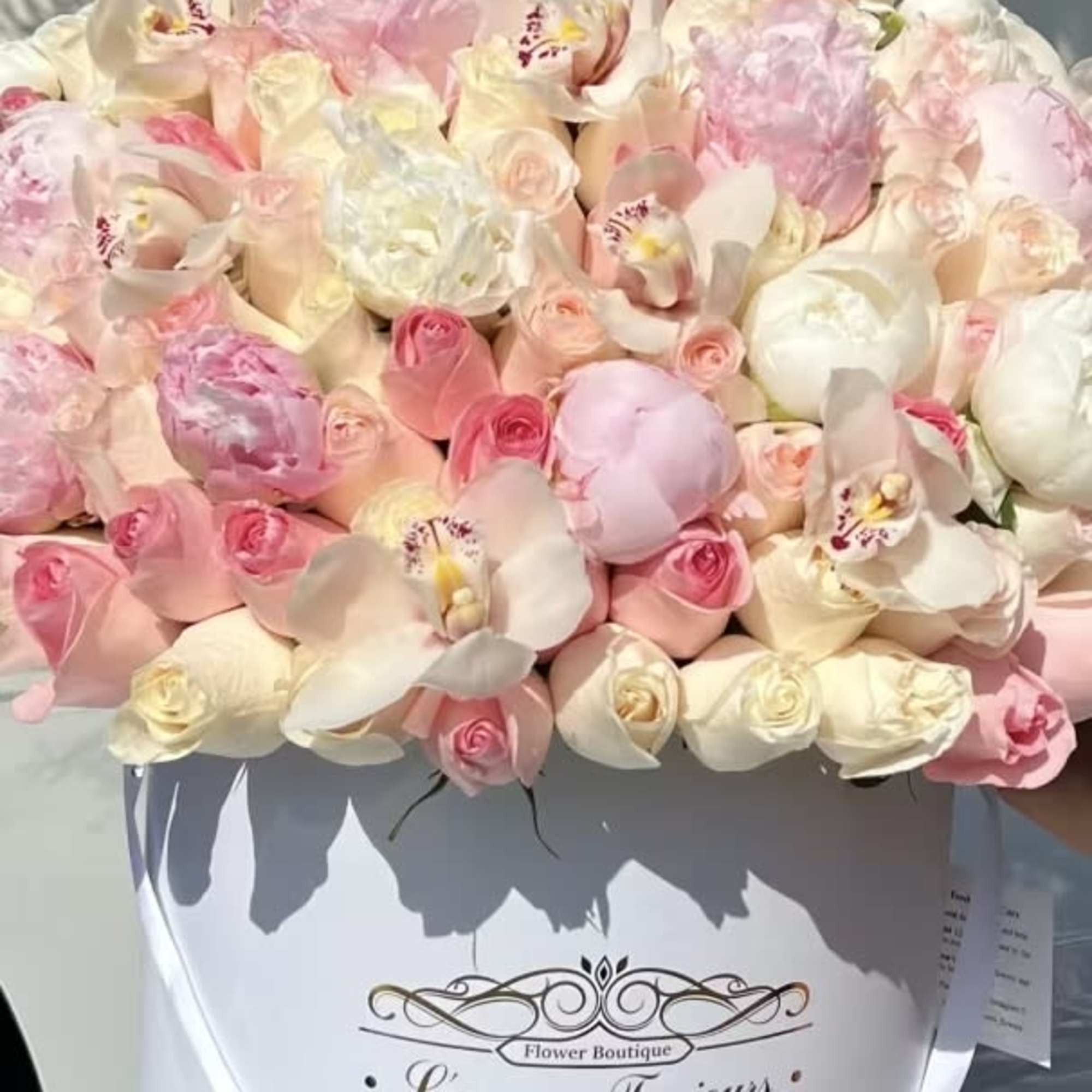 Pink and white bouquet of roses and orchids in a white hatbox
