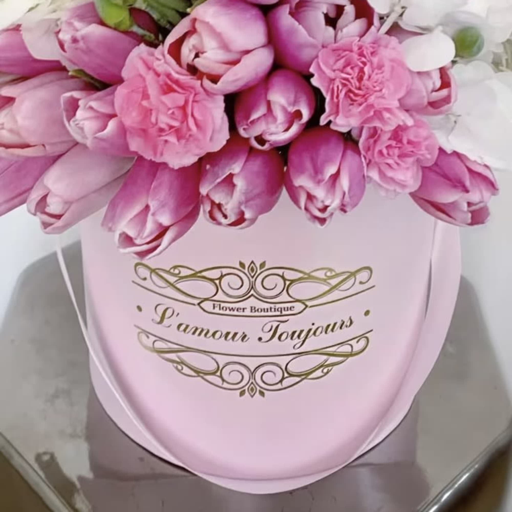 Pink tulips and roses arranged in a pale pink hat box with gold script
