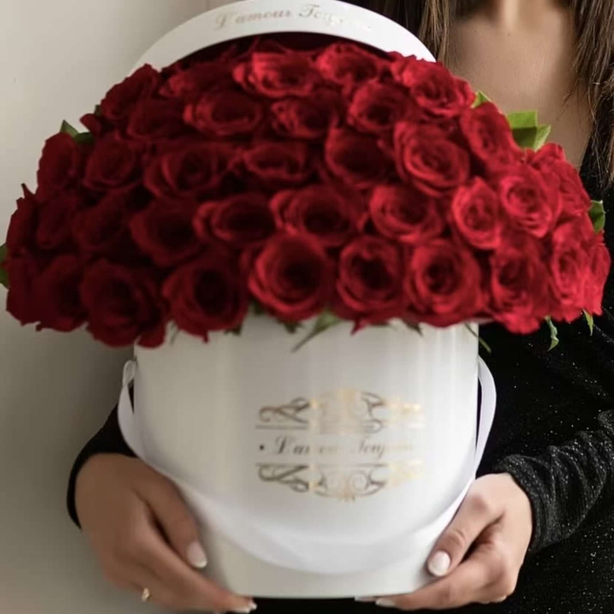 Large dome of red roses arranged in a white hatbox-style container held in both hands