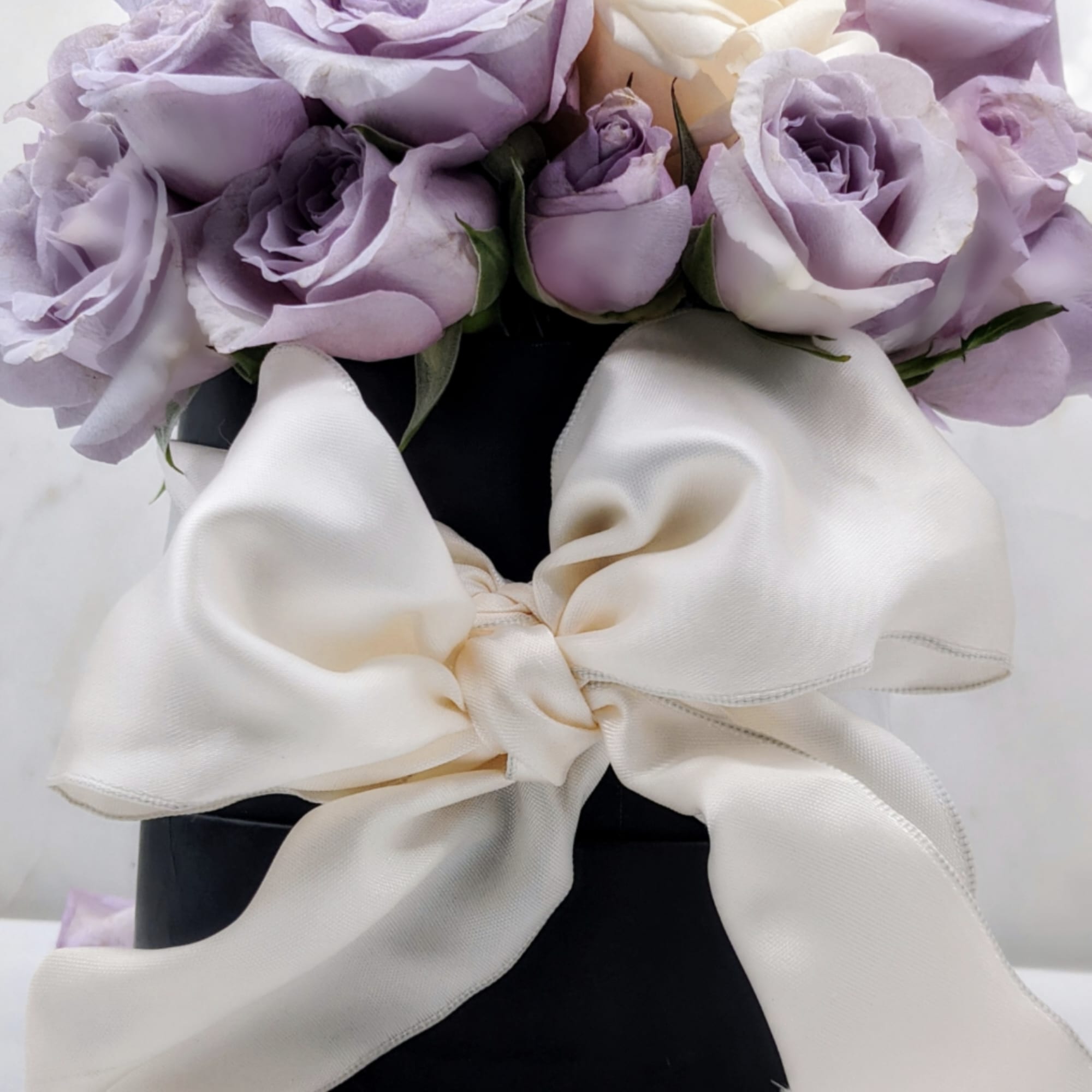 Lavender and white roses in a black box with a large ivory ribbon