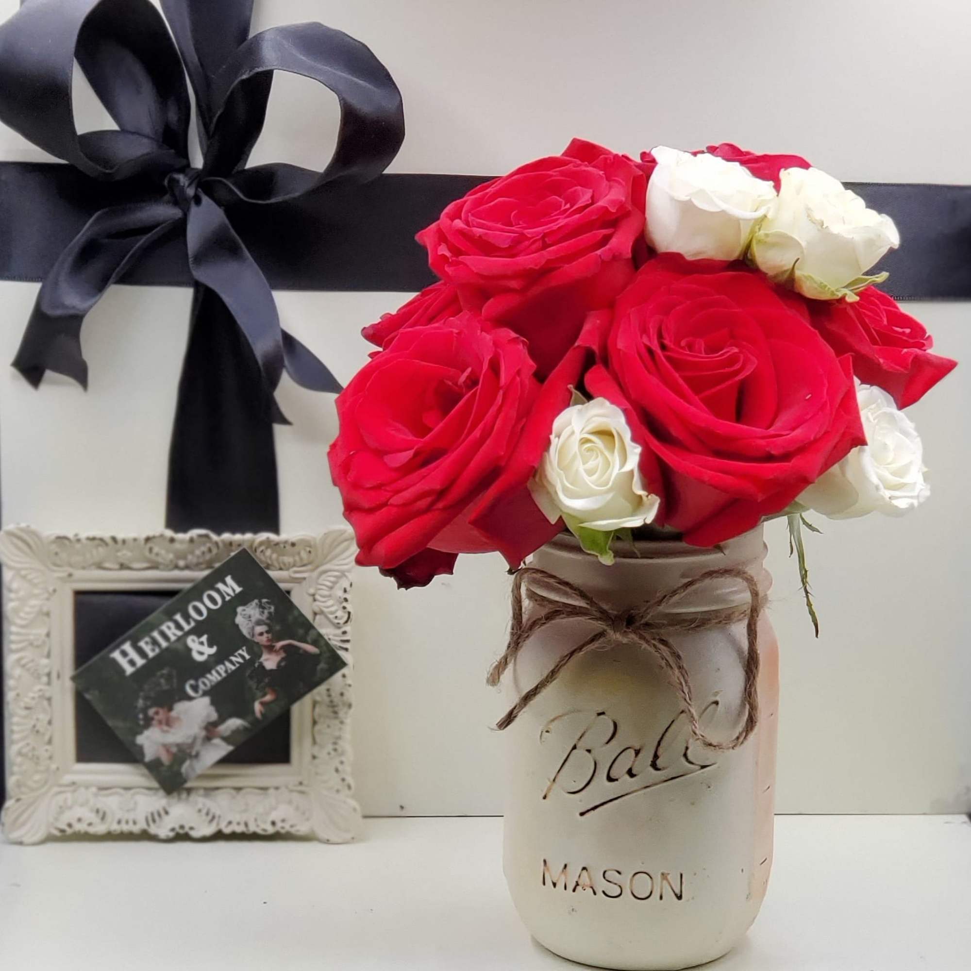 Red and white roses in a mason jar with a black ribbon bow