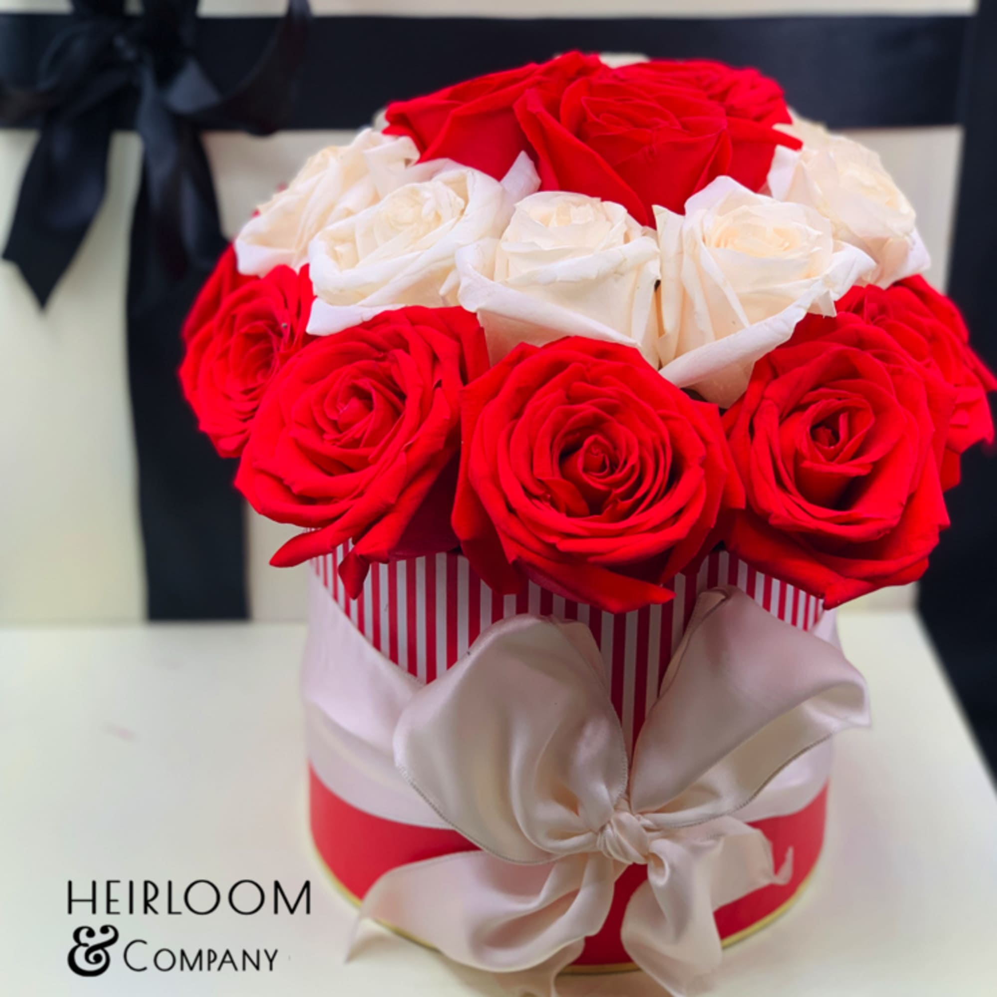 Red and white roses arranged in a round gift box with a satin bow