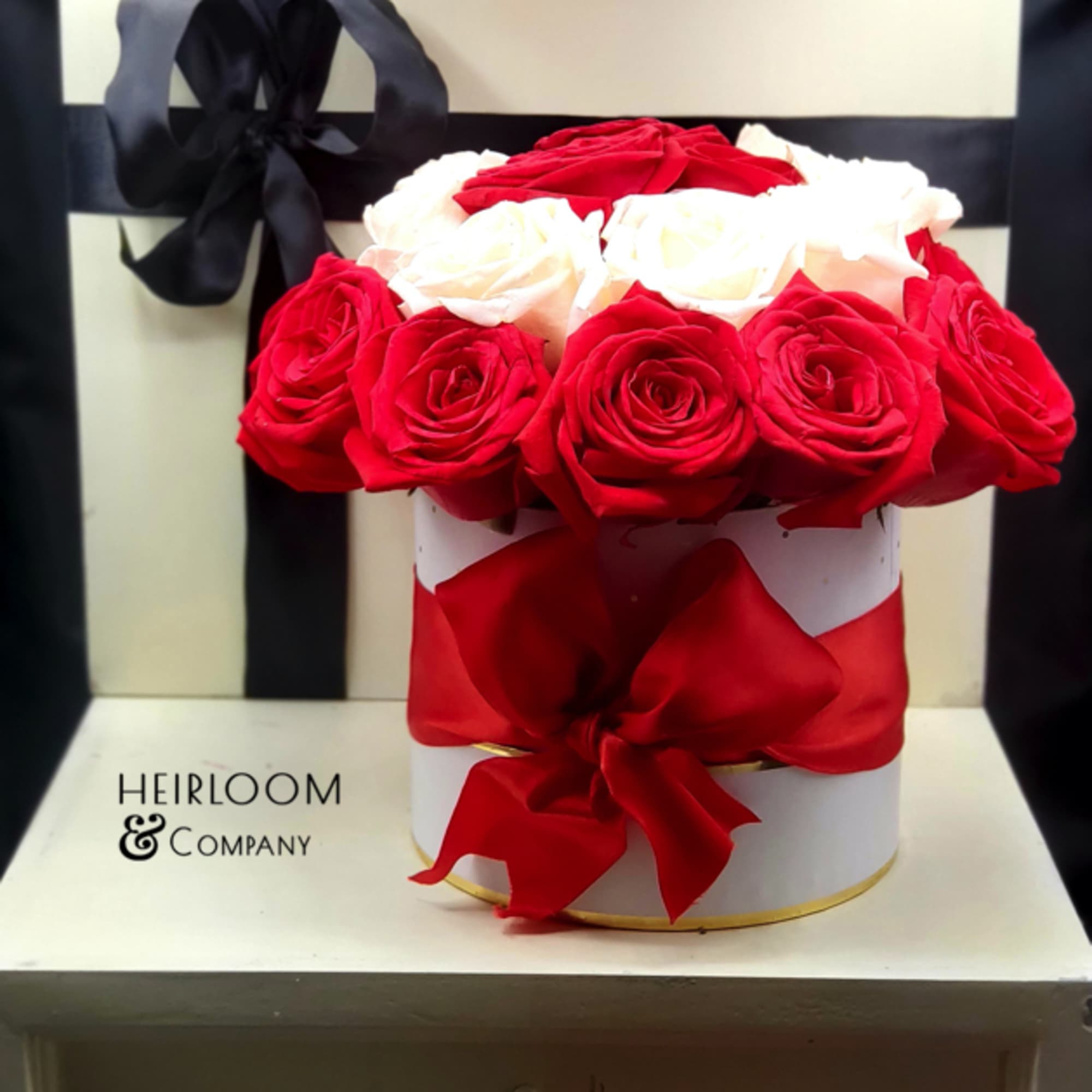 Red and white roses arranged in a round hat box with a black ribbon
