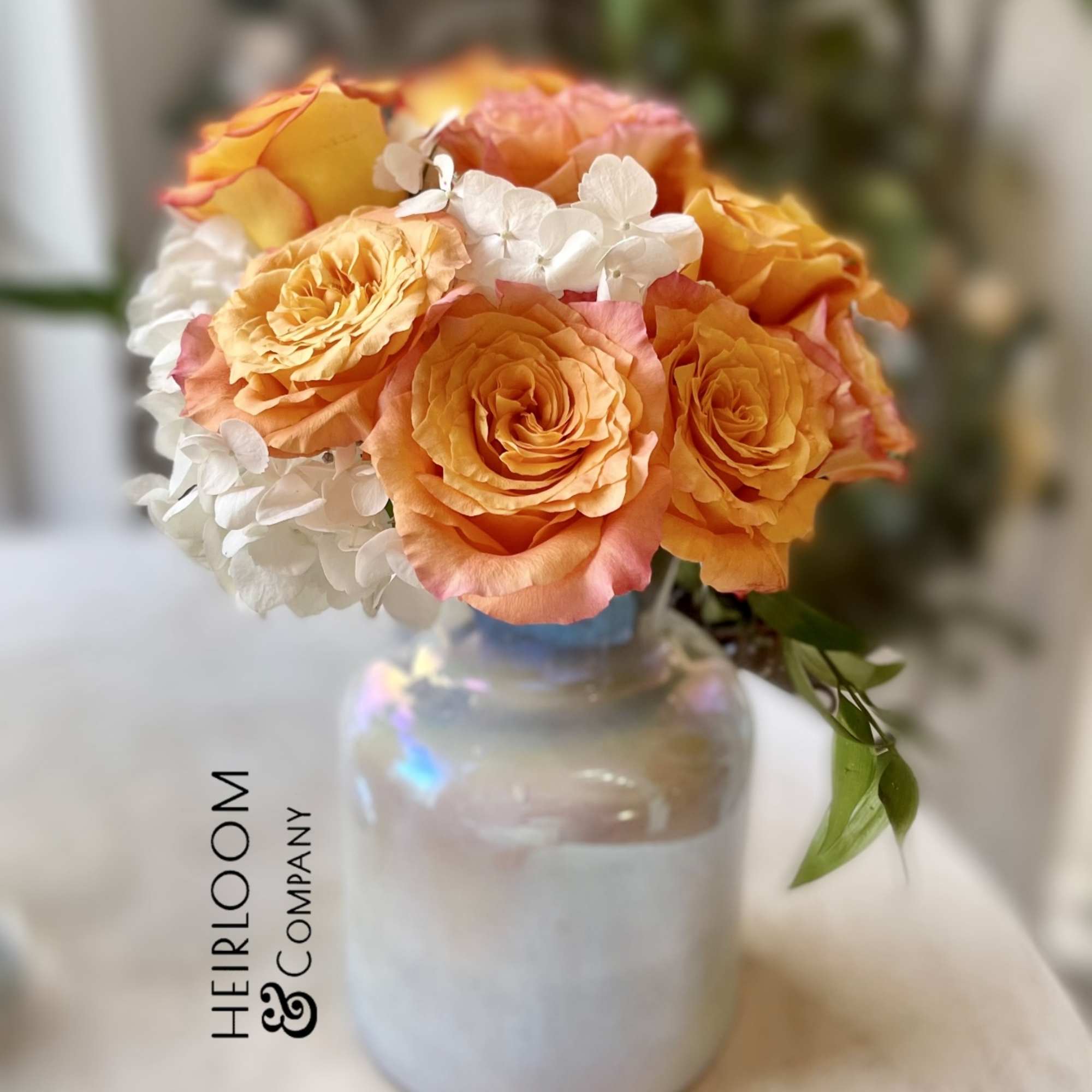 Orange roses and white hydrangeas arranged in a glass vase