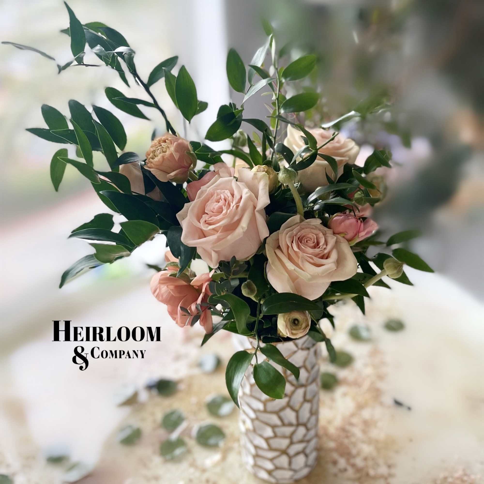 Blush roses arranged in a patterned white vase with dark green foliage