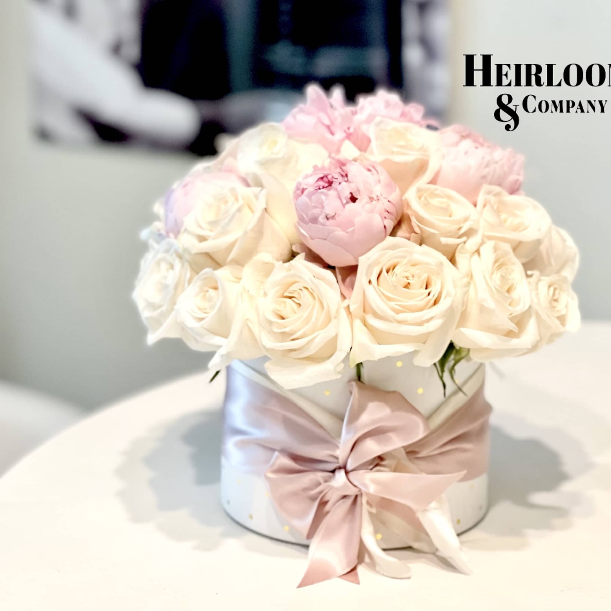 Pink and cream roses arranged in a round box with a satin ribbon