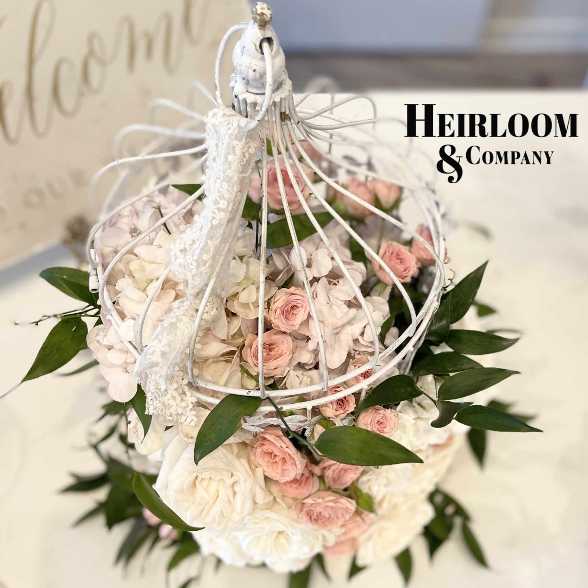 Pink and white roses arranged in a white birdcage with greenery