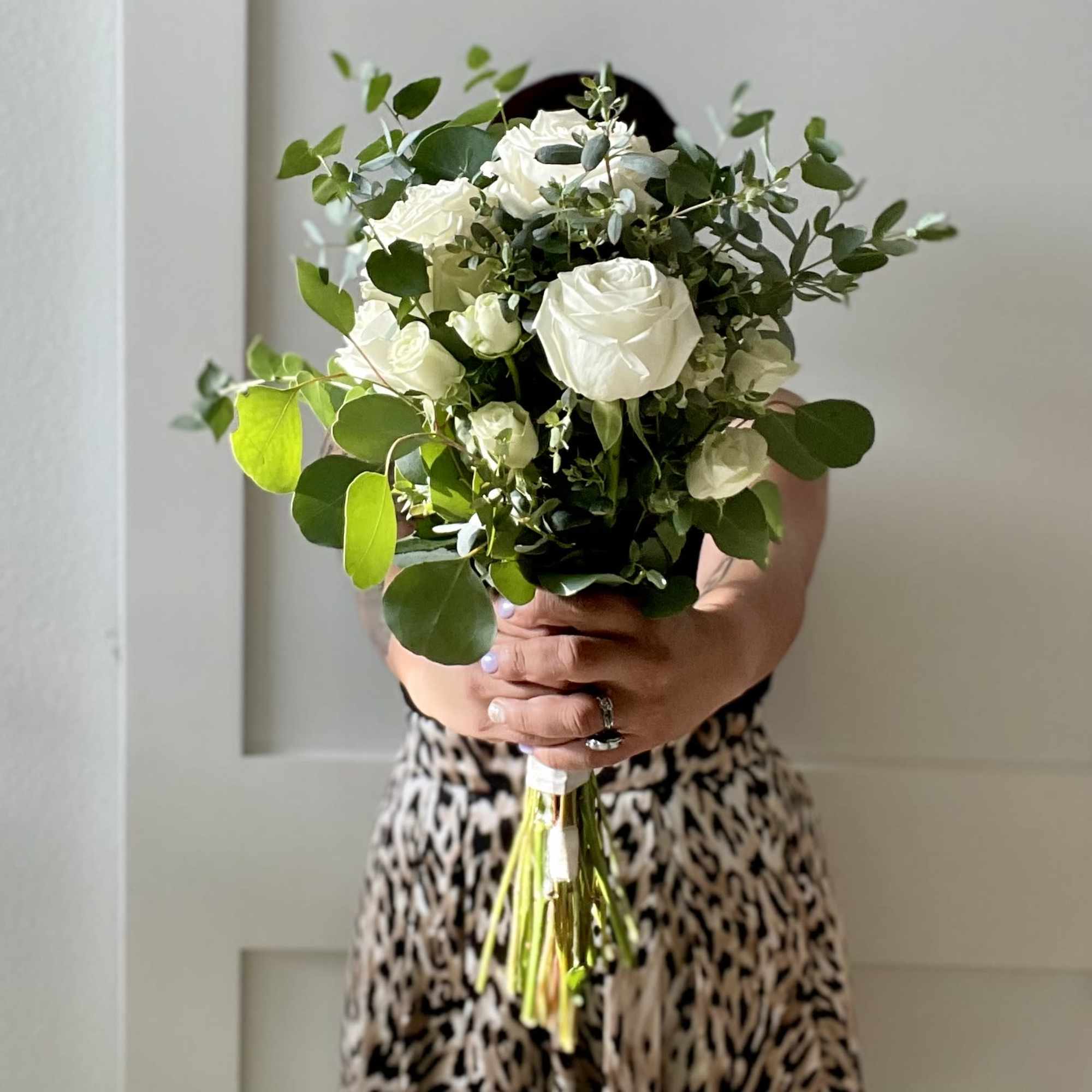Bouquet of white roses with greenery held in both hands