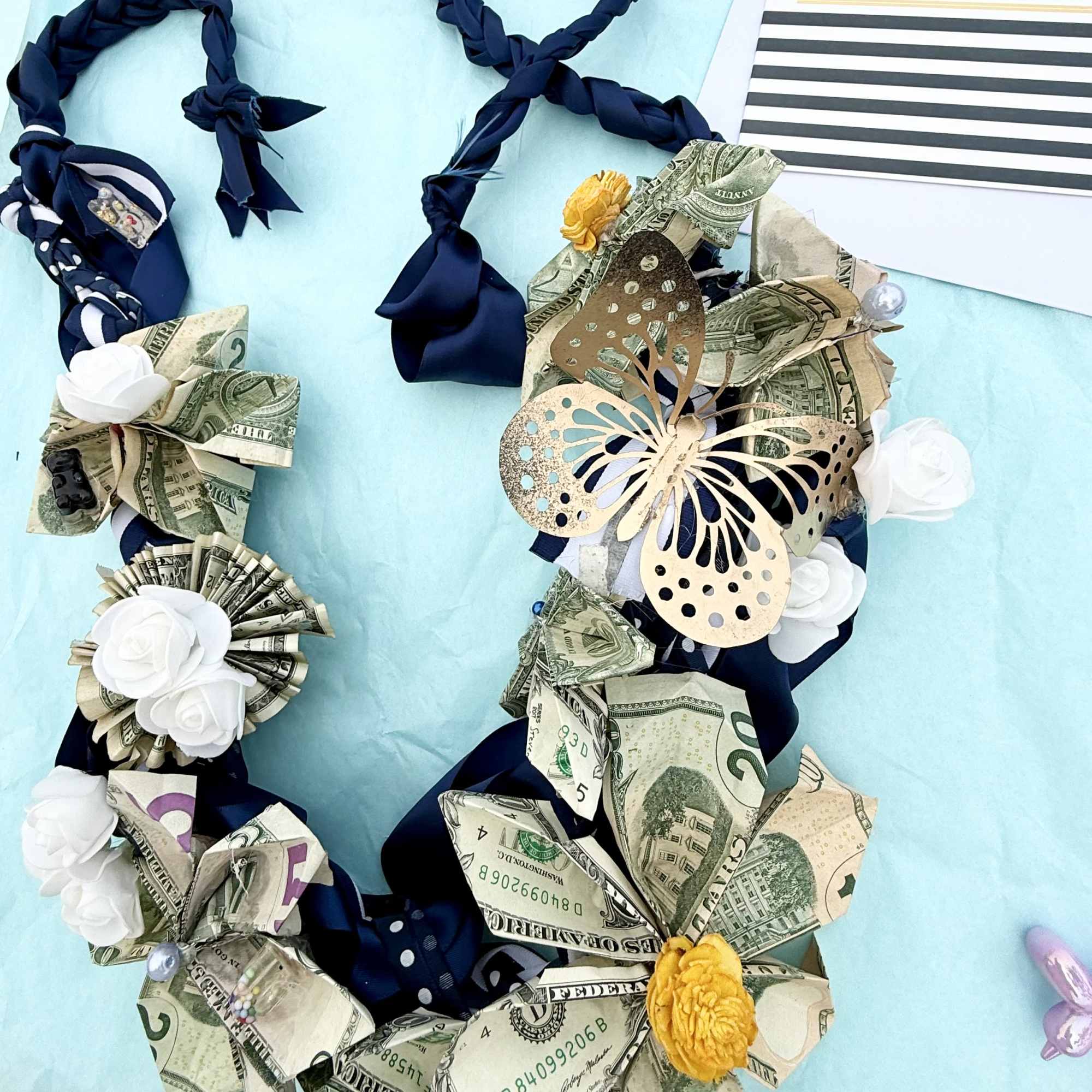 Money lei with ribbon and paper flowers beside a graduation card