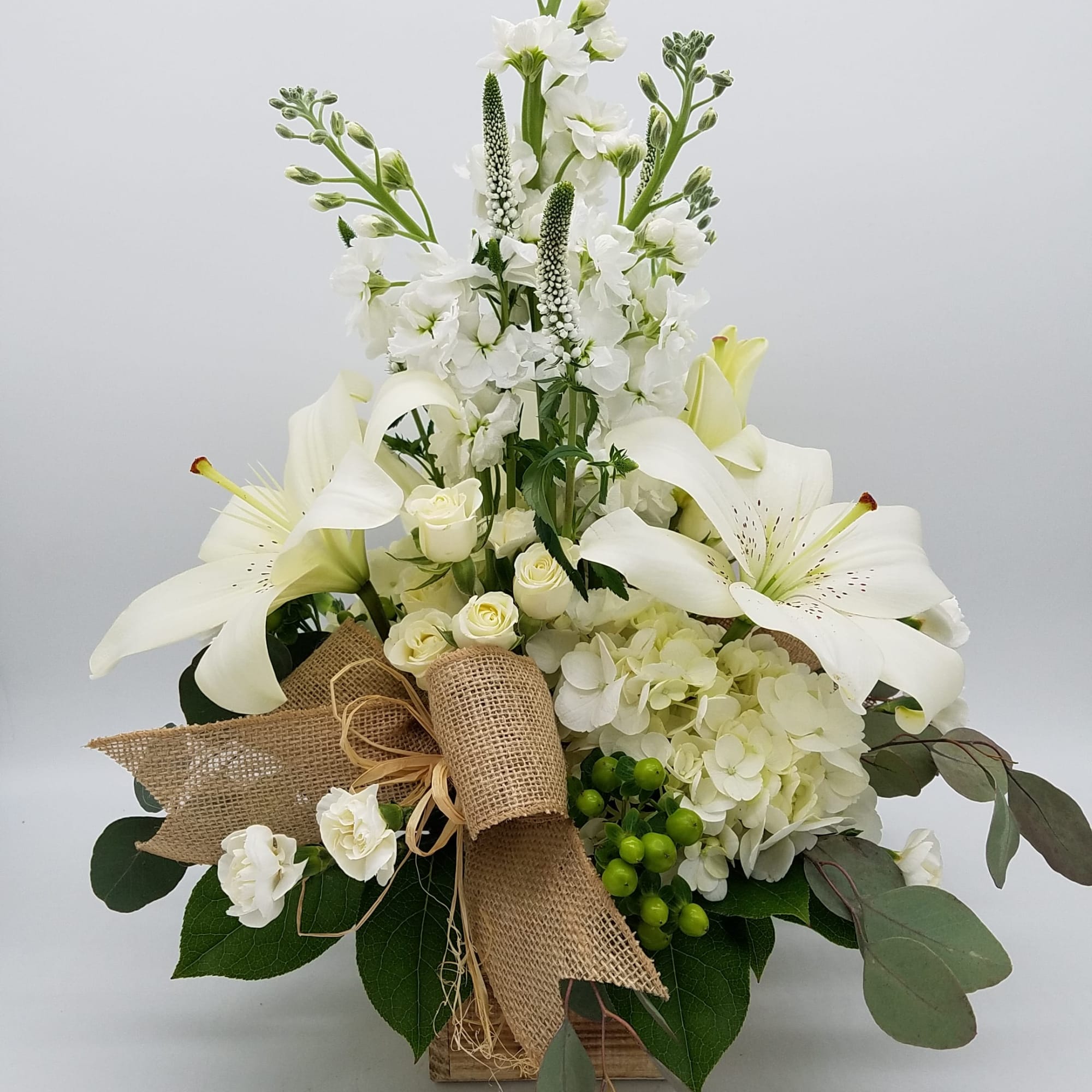 White lilies and roses arranged in a burlap-wrapped box