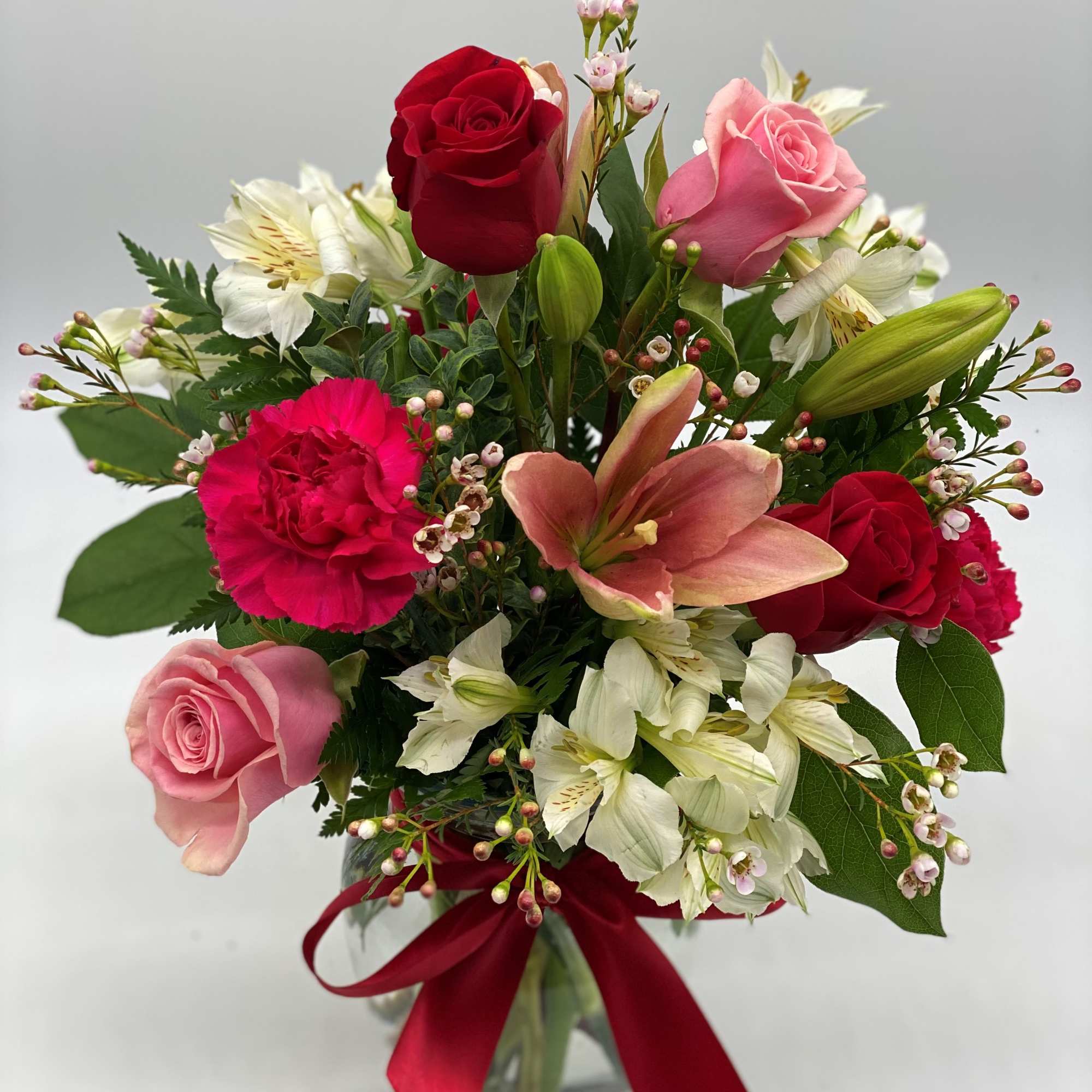 Mixed bouquet of roses, lilies, and carnations in a glass vase with a red ribbon, photo 2 of 3