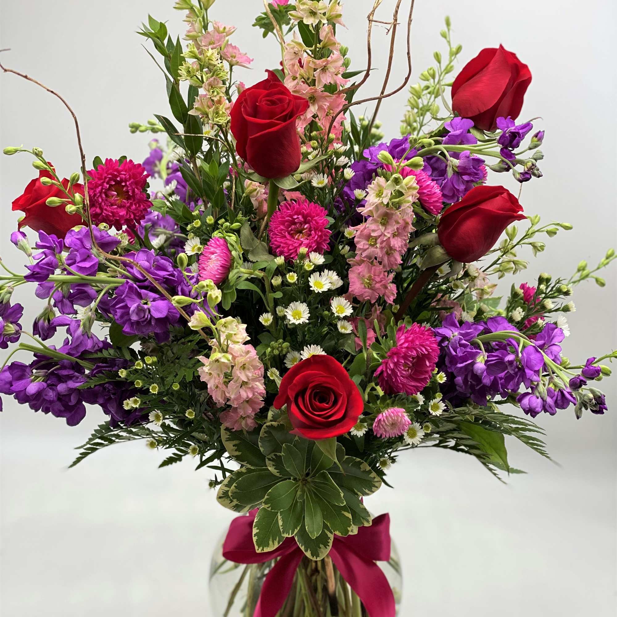 Bouquet of red roses, purple blooms, and pink flowers in a glass vase