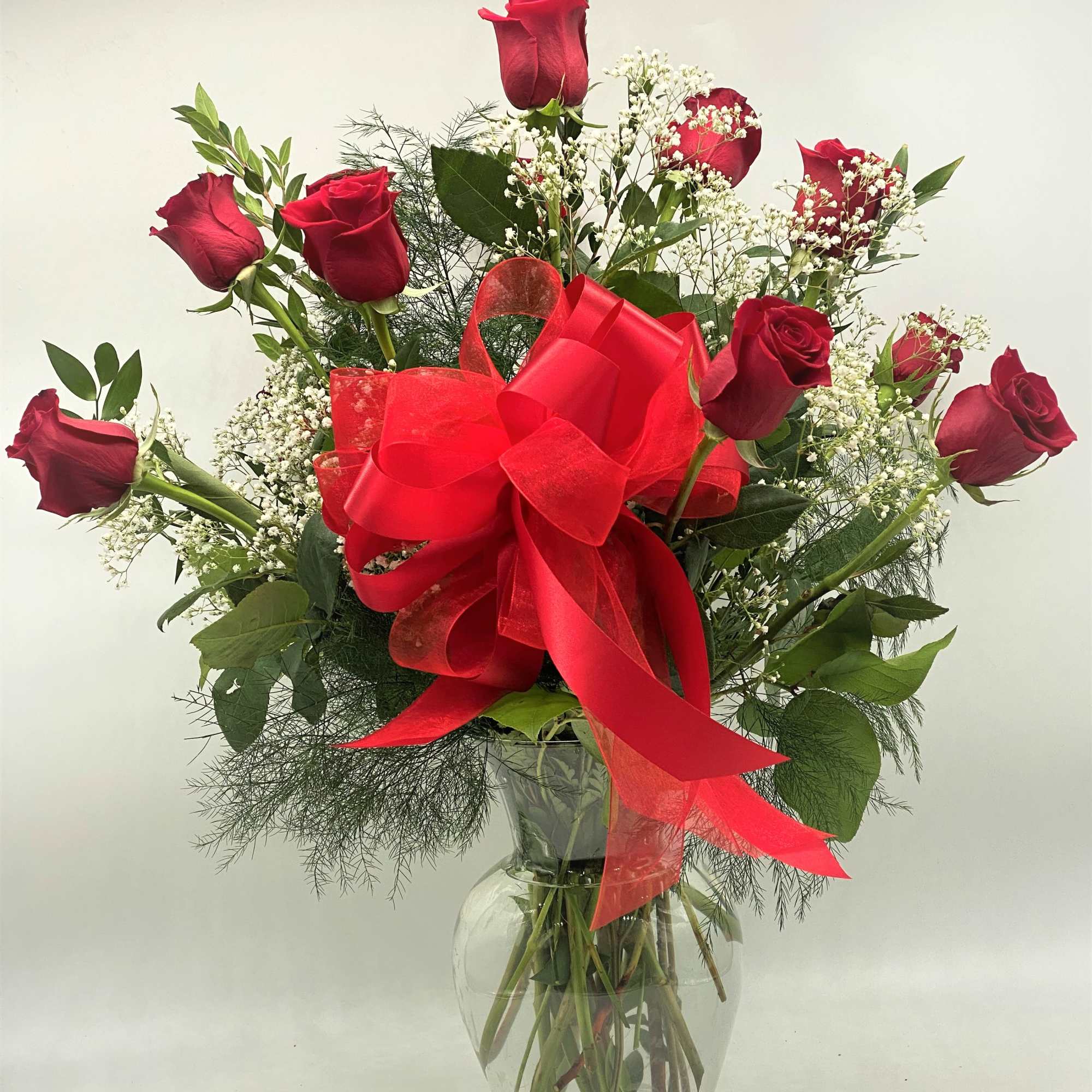 Red roses in a clear glass vase with a large red bow