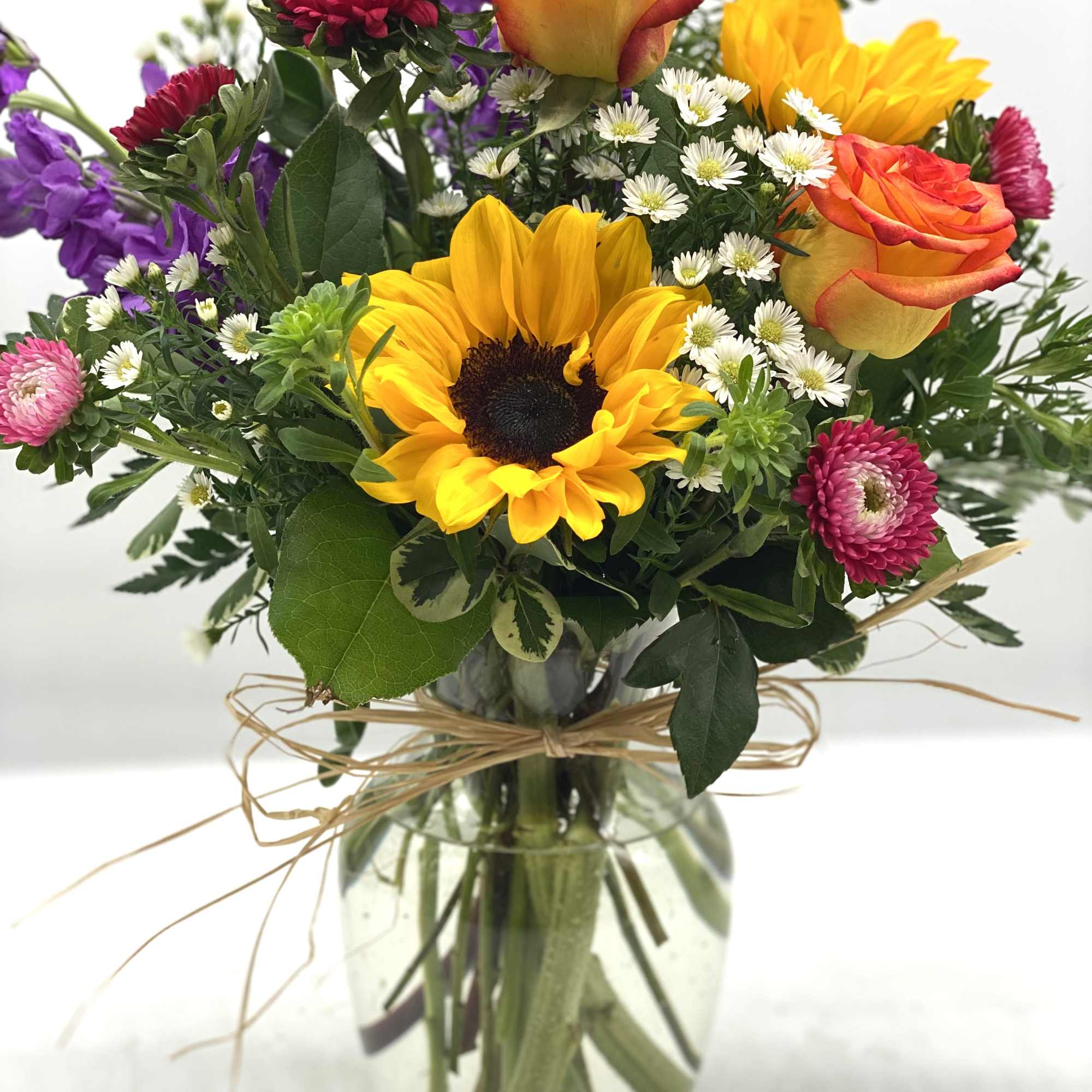 Mixed bouquet with sunflowers, roses, and daisies in a glass vase