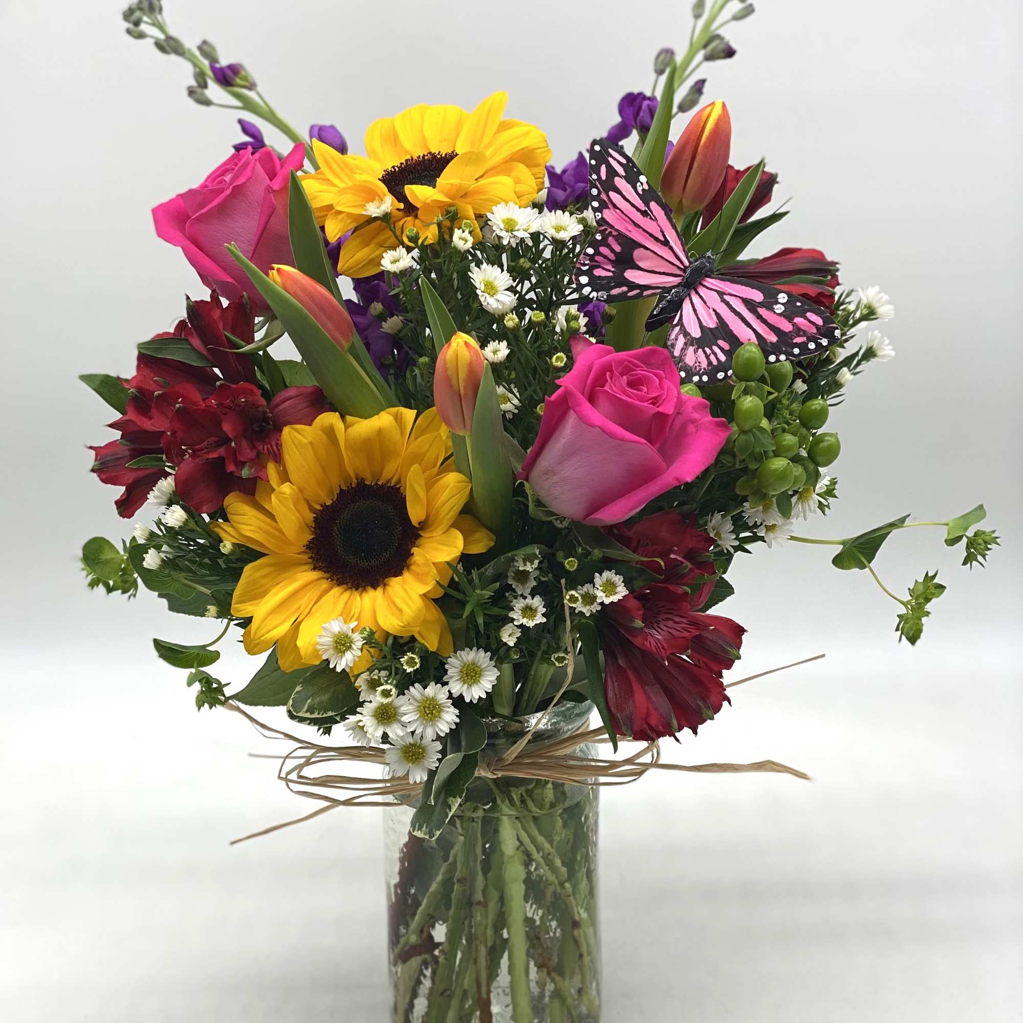 Bouquet of sunflowers, pink roses, and red flowers in a glass vase