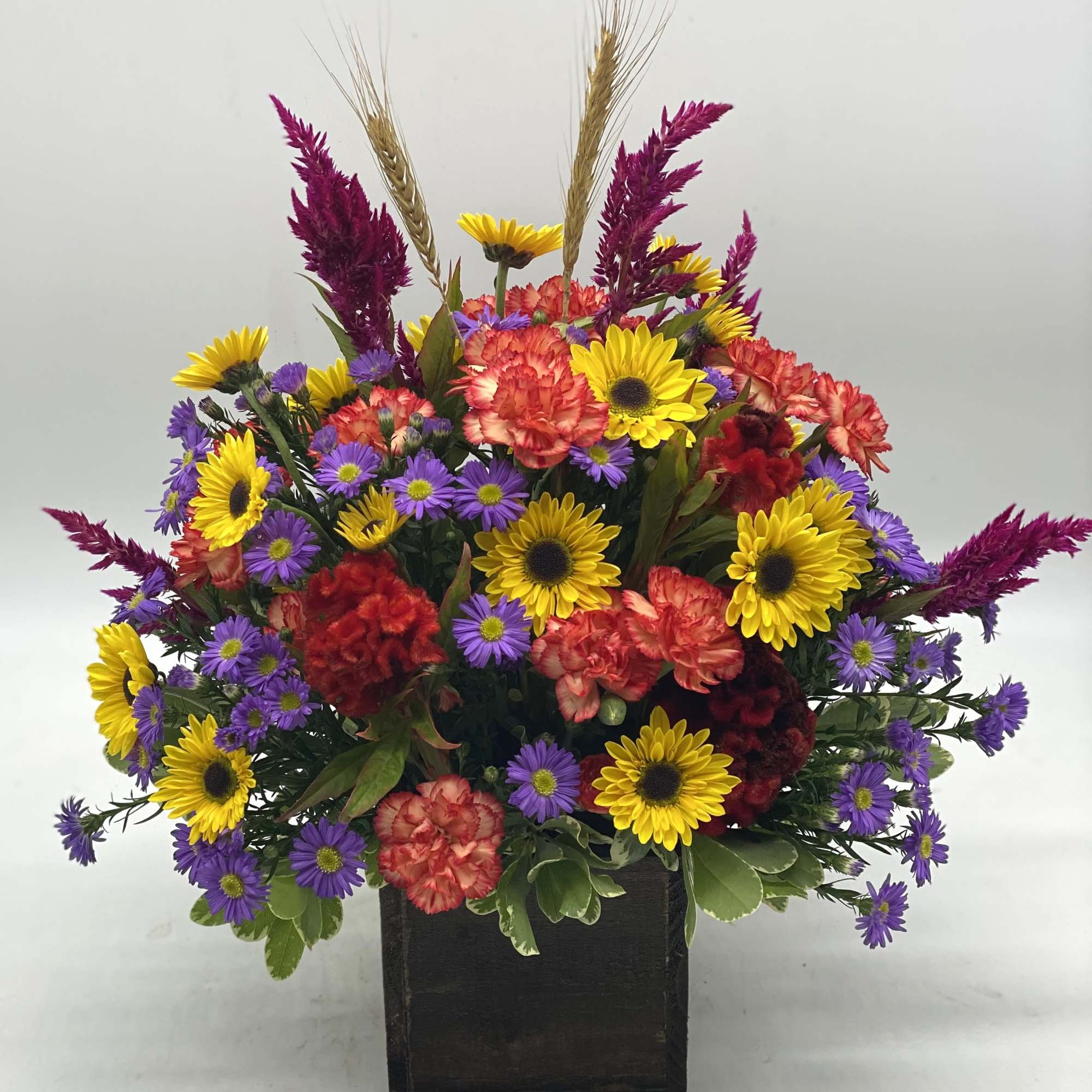 A bright mix of fresh, fall toned flowers designed in a wooden