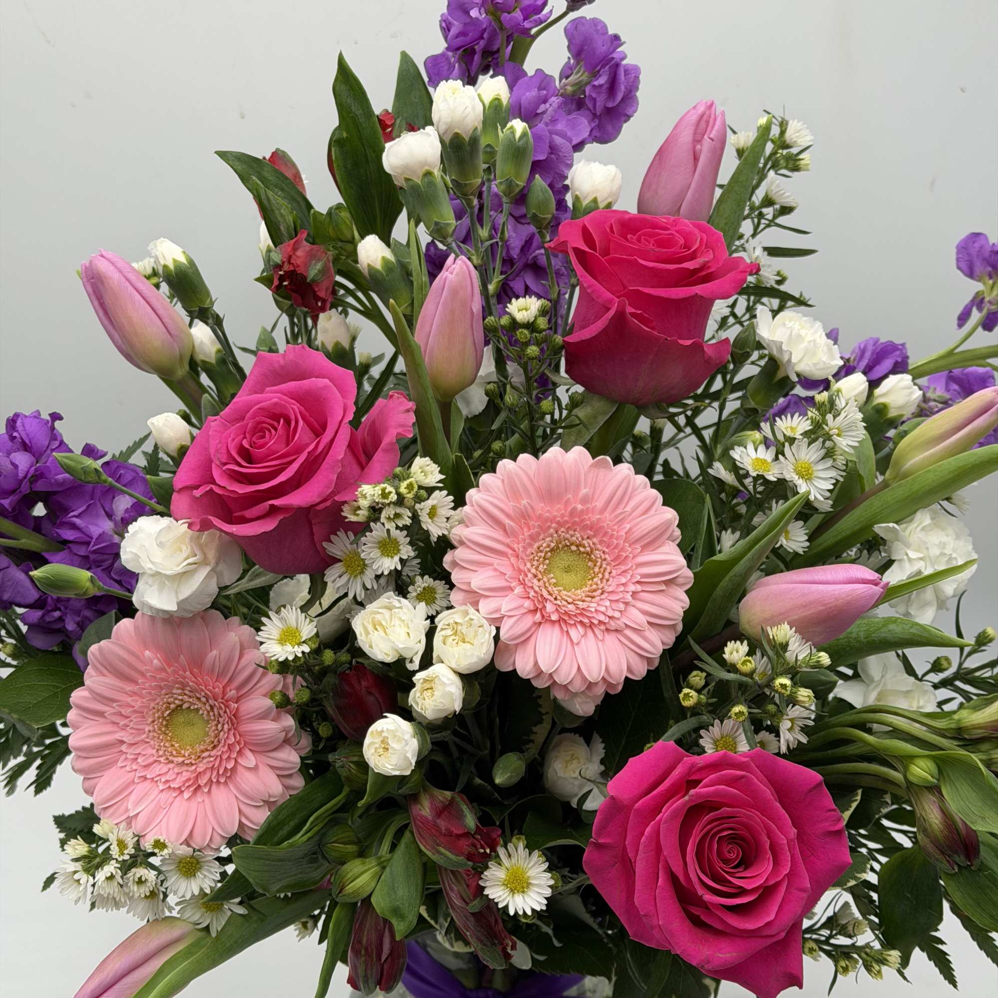 Bouquet of pink roses, gerbera daisies, and purple flowers tied with a ribbon