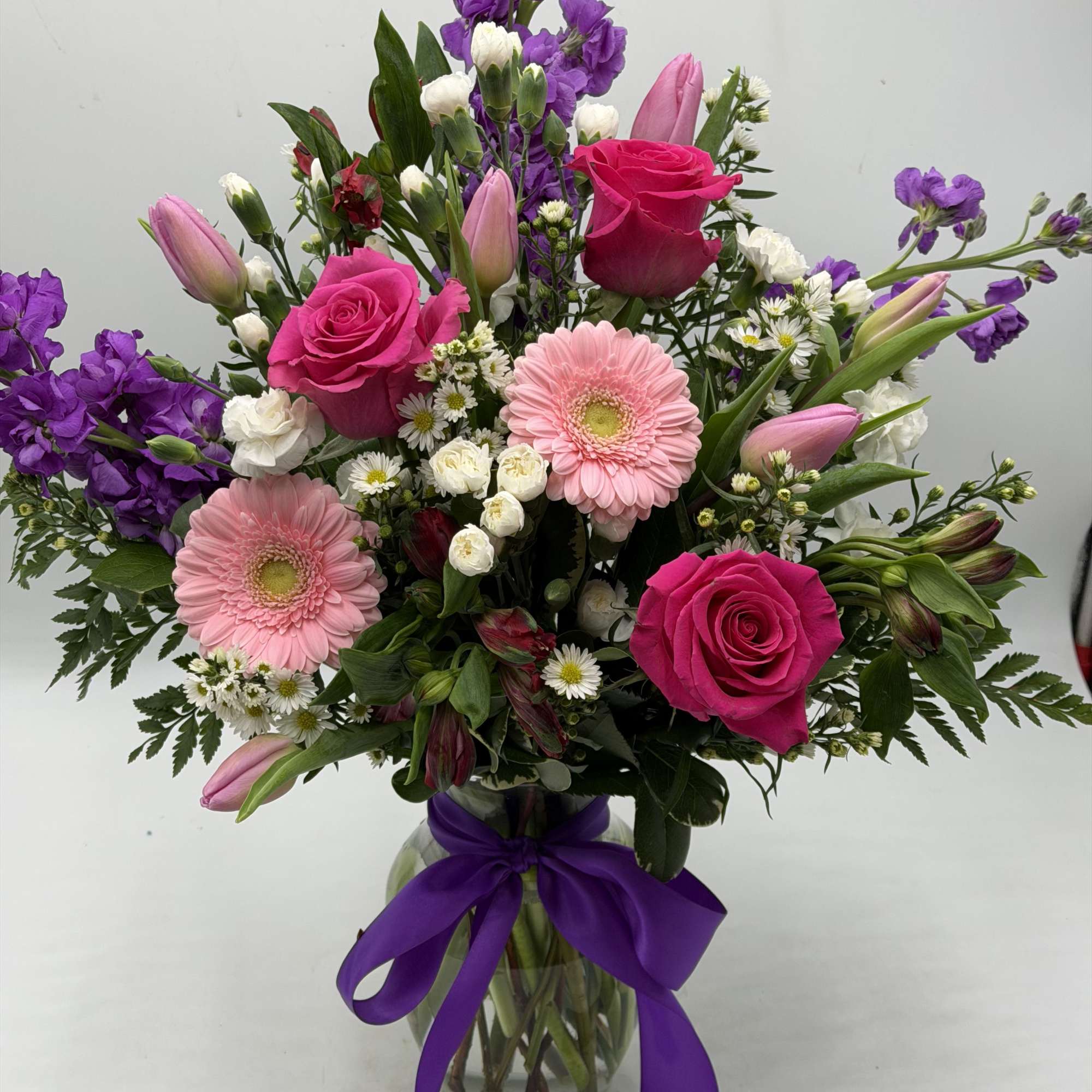 Bouquet of pink roses, gerbera daisies, and purple flowers in a glass vase