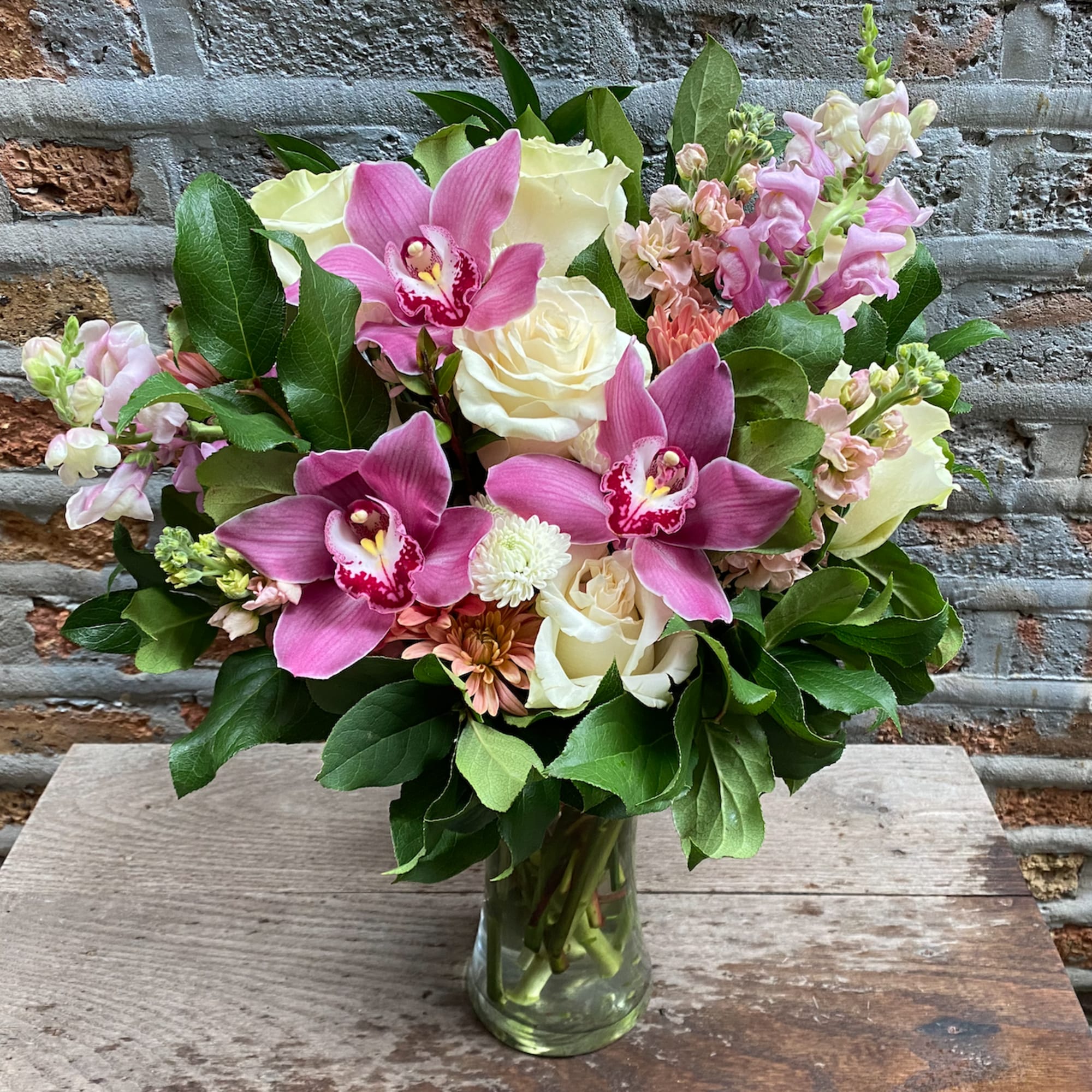 Vase arrangement of pink orchids, white roses, and pastel blooms in a clear glass cylinder