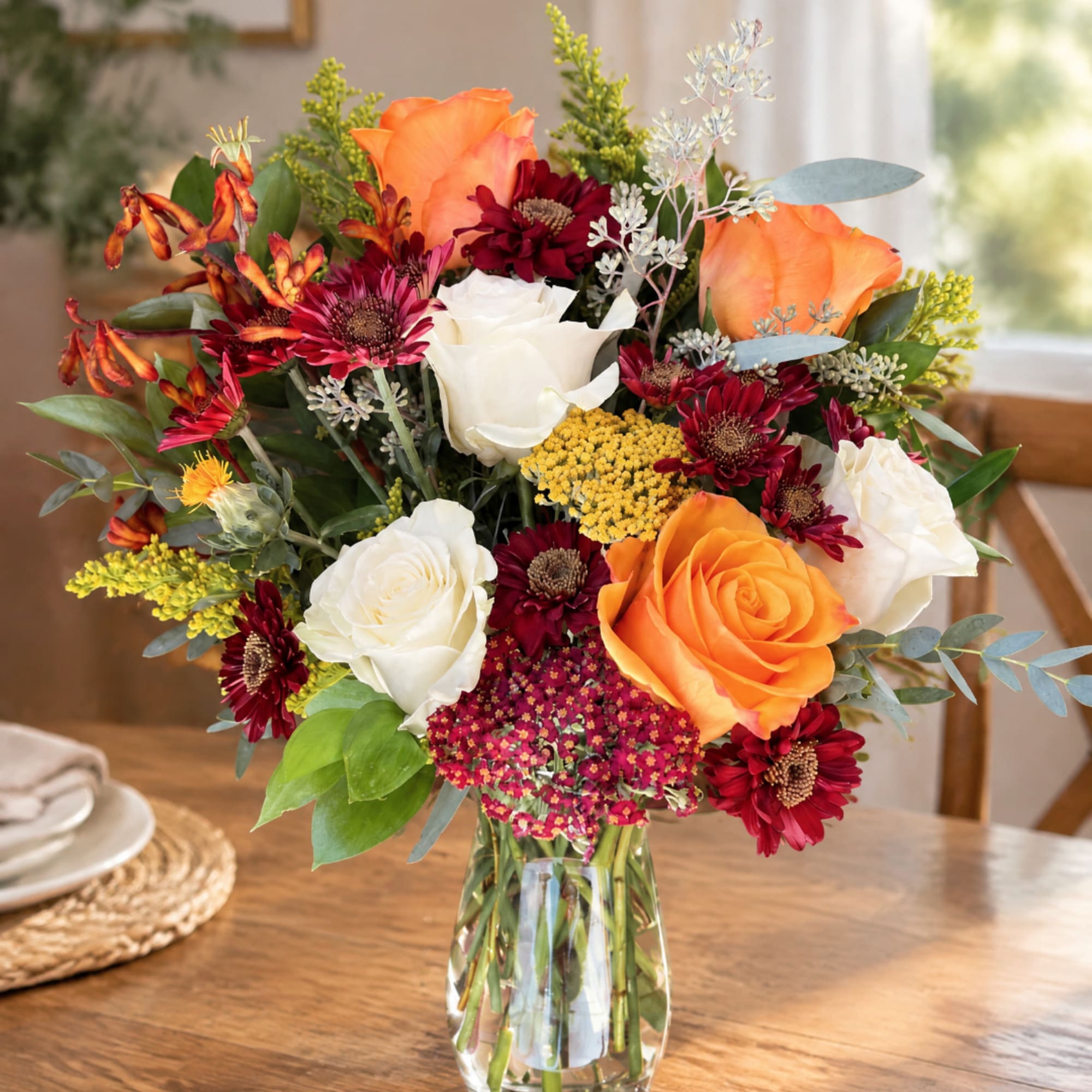 Mixed bouquet of orange and white roses with burgundy daisies in a glass vase