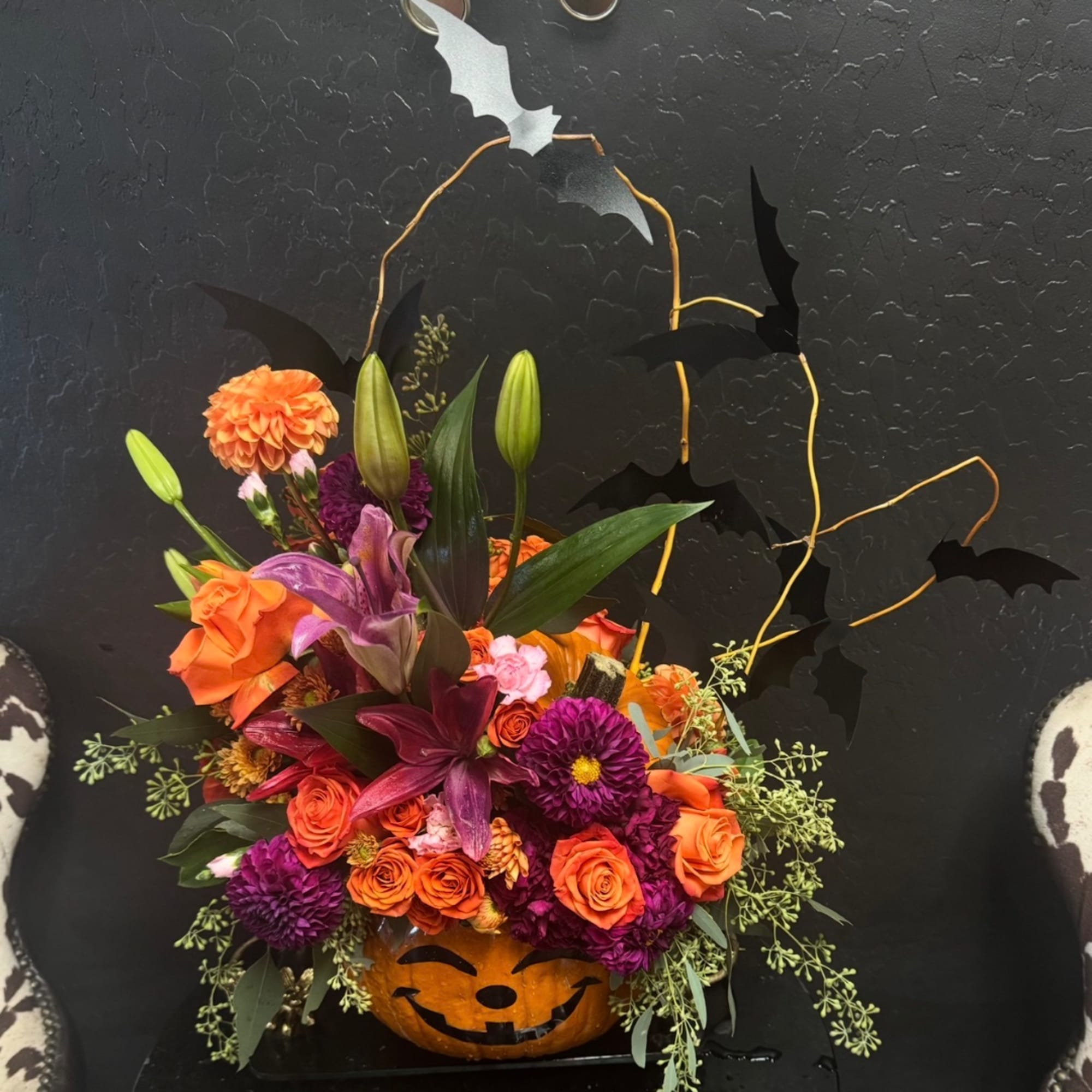 Orange and purple floral arrangement in a carved pumpkin container with bat decorations