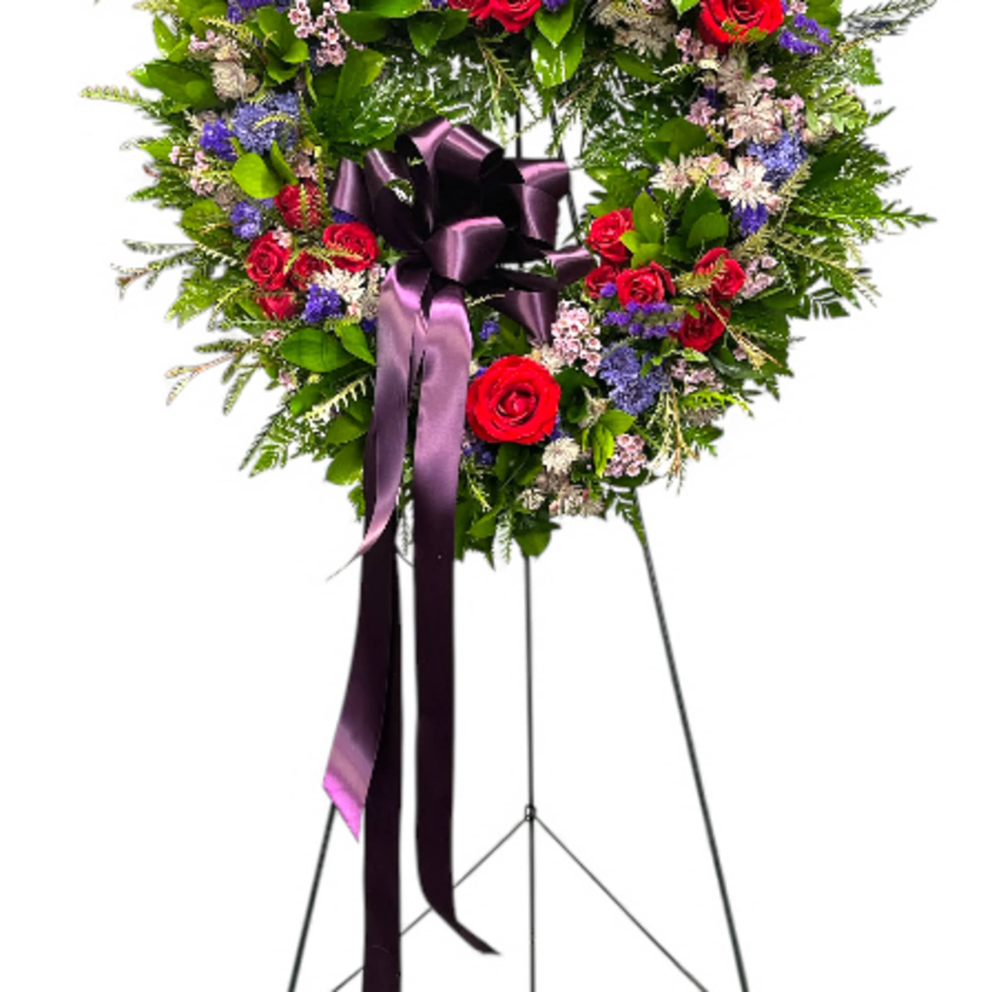Heart-shaped floral wreath with red roses and a purple ribbon on a stand